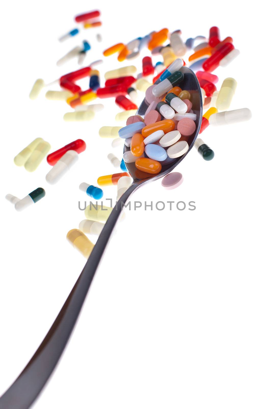 A lot of colored pills and tabs with a spoon over a white background