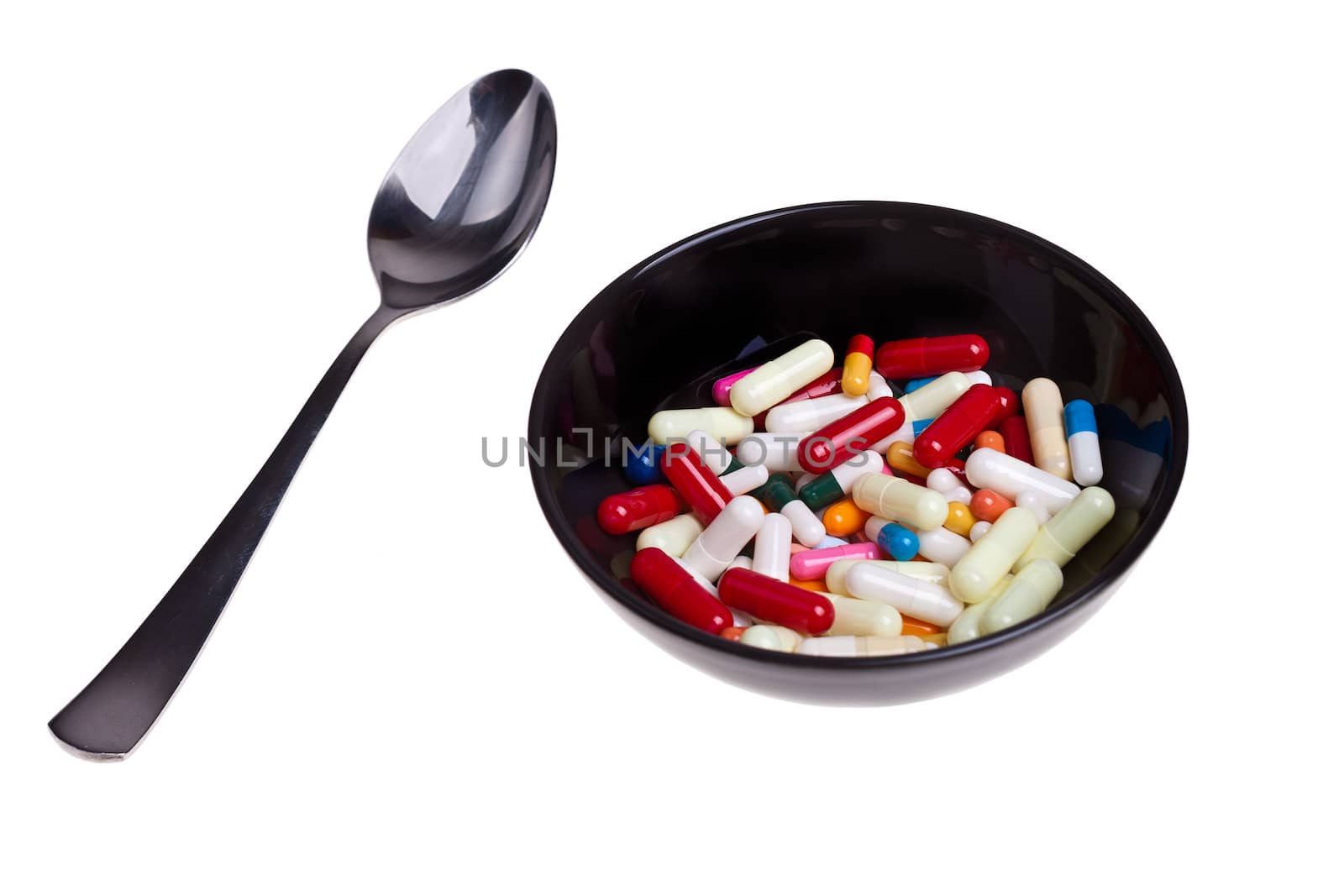 Many colored pills and capsules in a bowl with a spoon