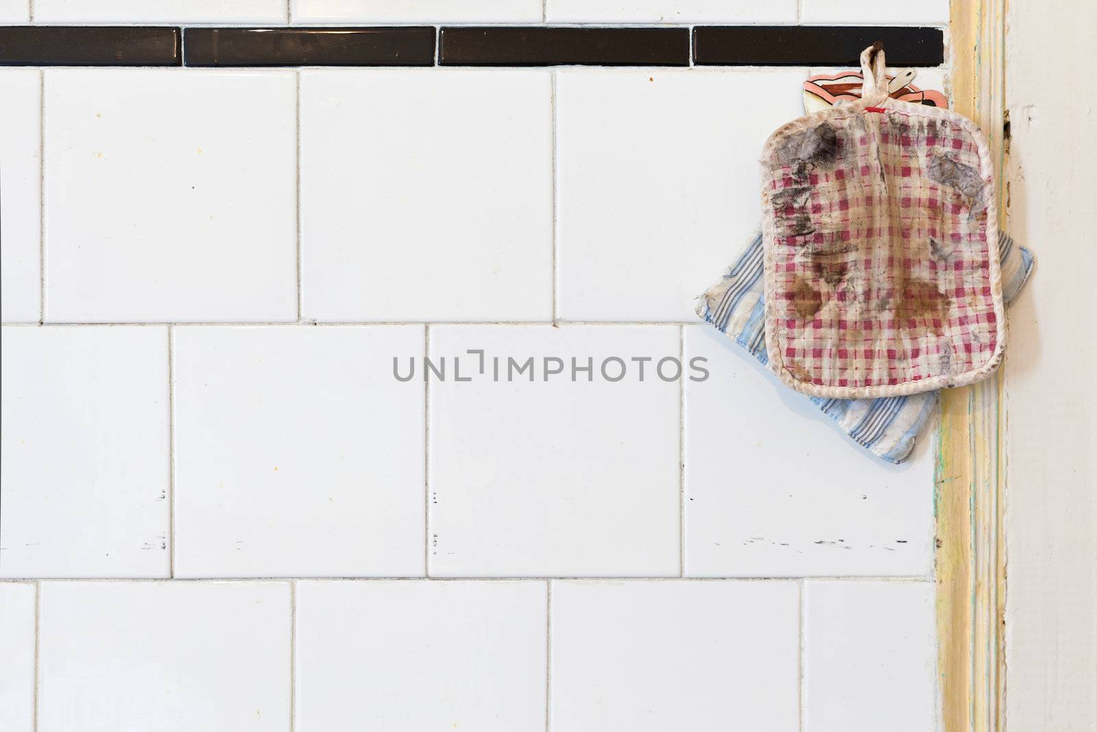 Two Old Oven Mitts on a dirty whiter tiled kitchen wall. Lot of Copy Space