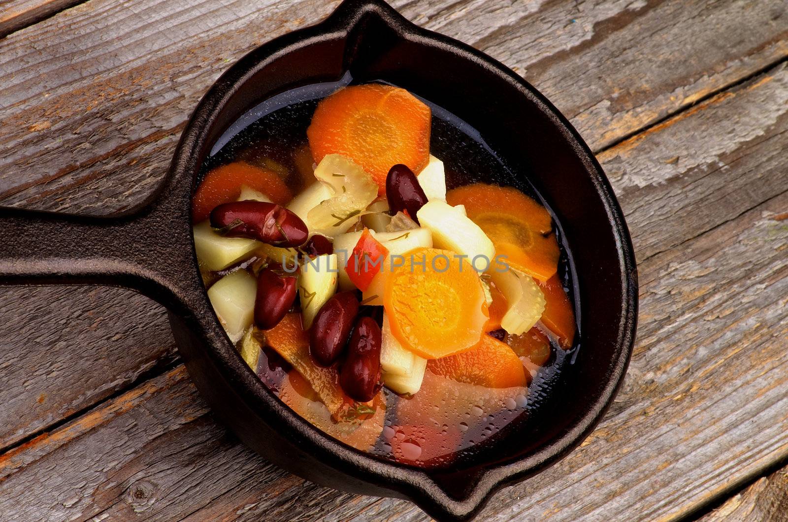 Vegetable Stew with Red Bean and Carrot, Potato, Celery, Greens and Bouillon in Black Stewpot isolated on Wooden background. Top View