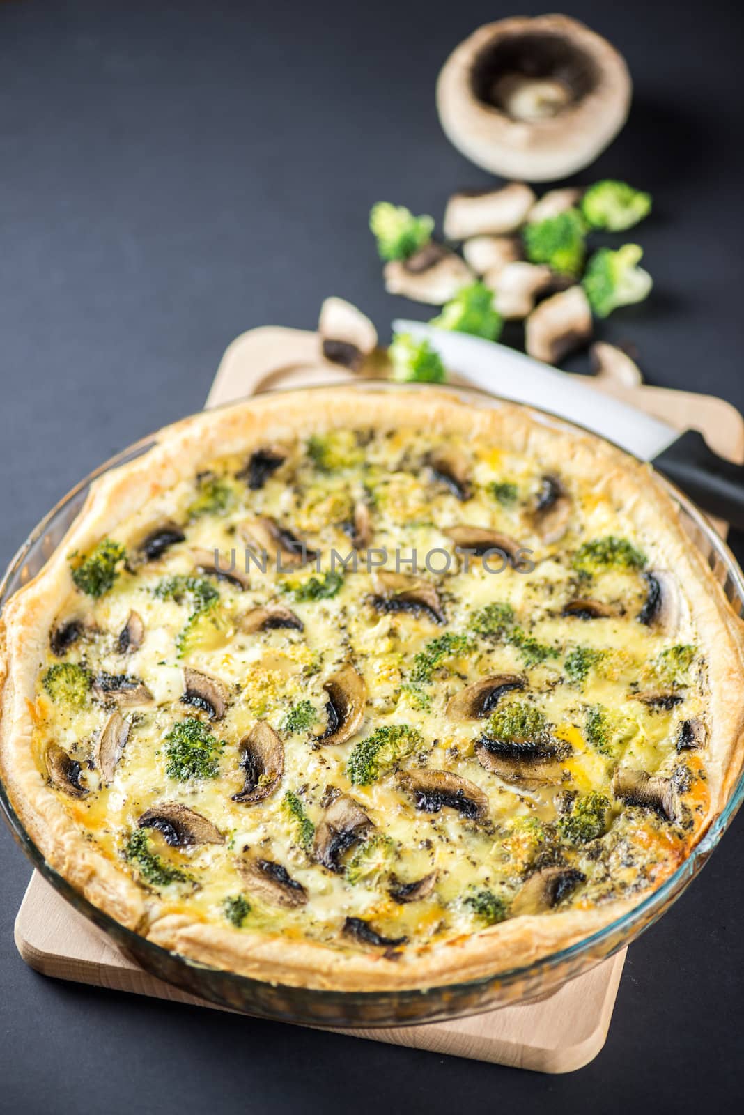 Delicious mushroom quiche on black background with knife