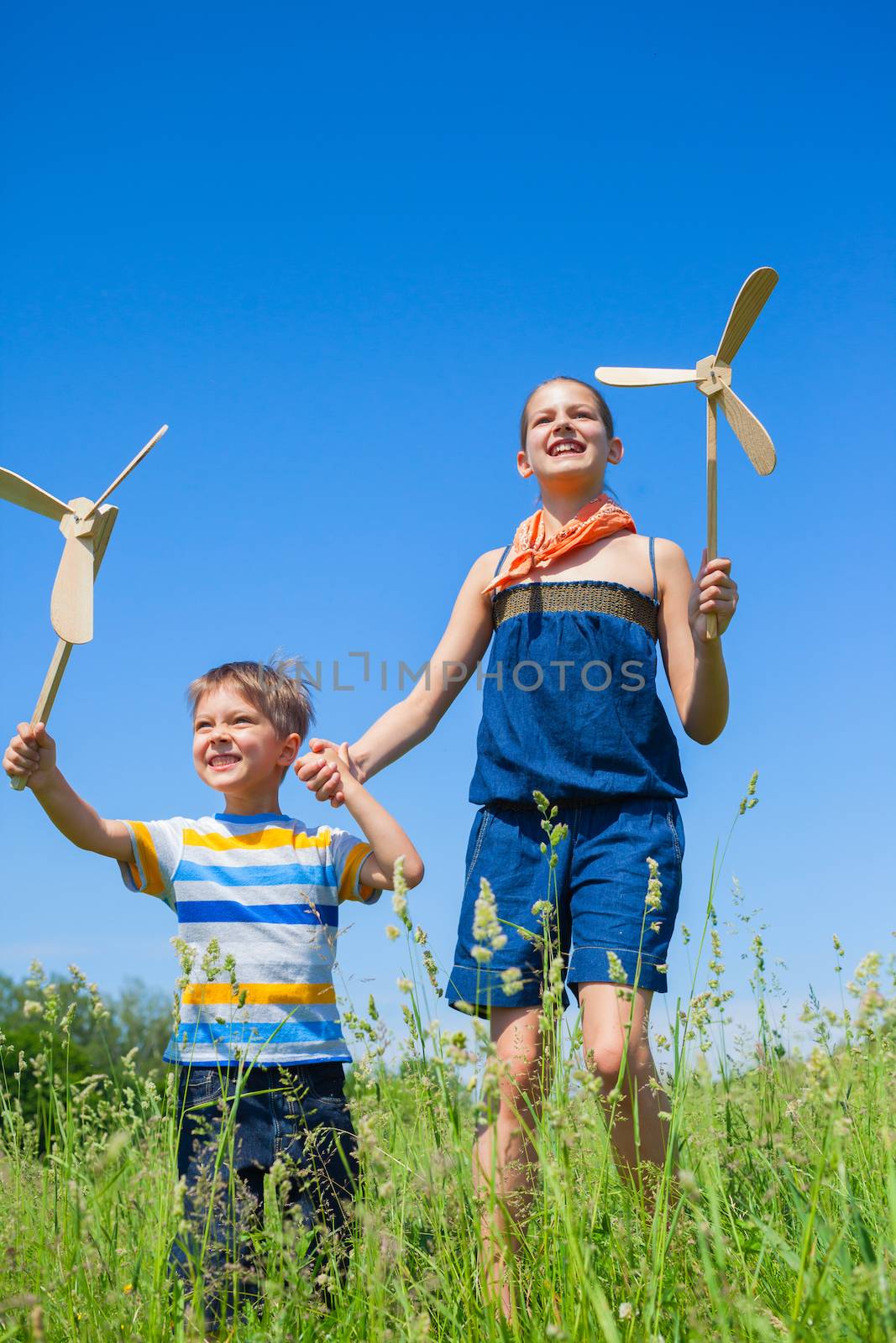 Cute kids runing on grass in summer day holds wooden windmill in hand