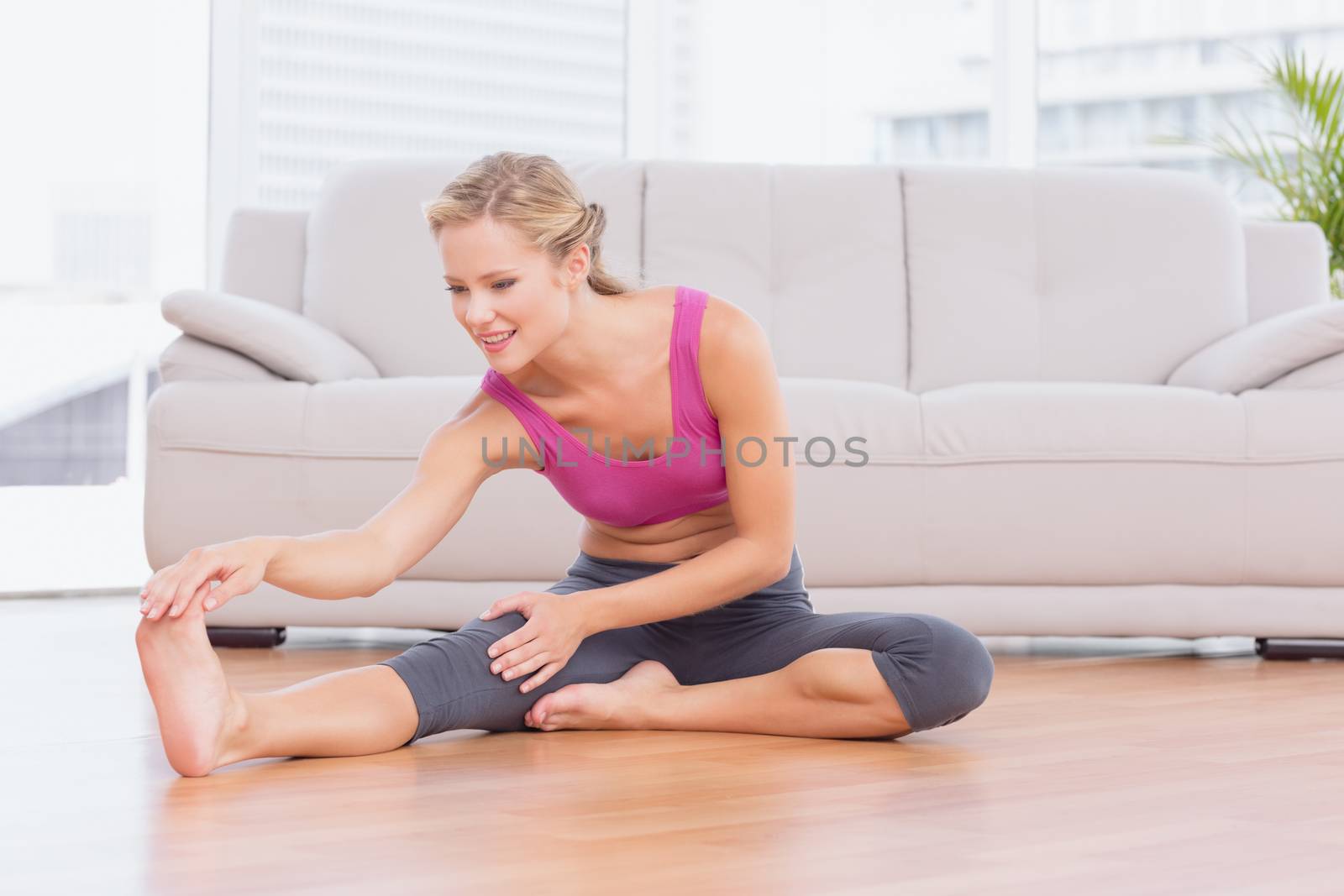 Fit blonde sitting on floor stretching her leg at home in the living room