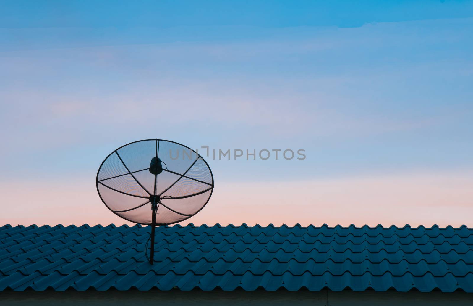 Silhouetted satellite dish on the roof in sunset sky