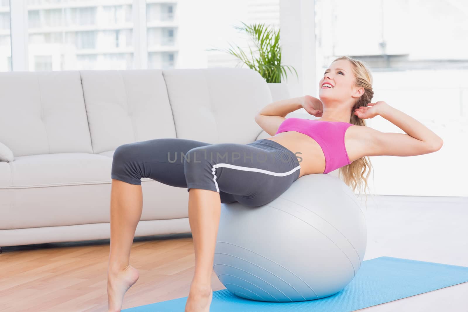 Smiling blonde doing sit ups with exercise ball at home in the living room