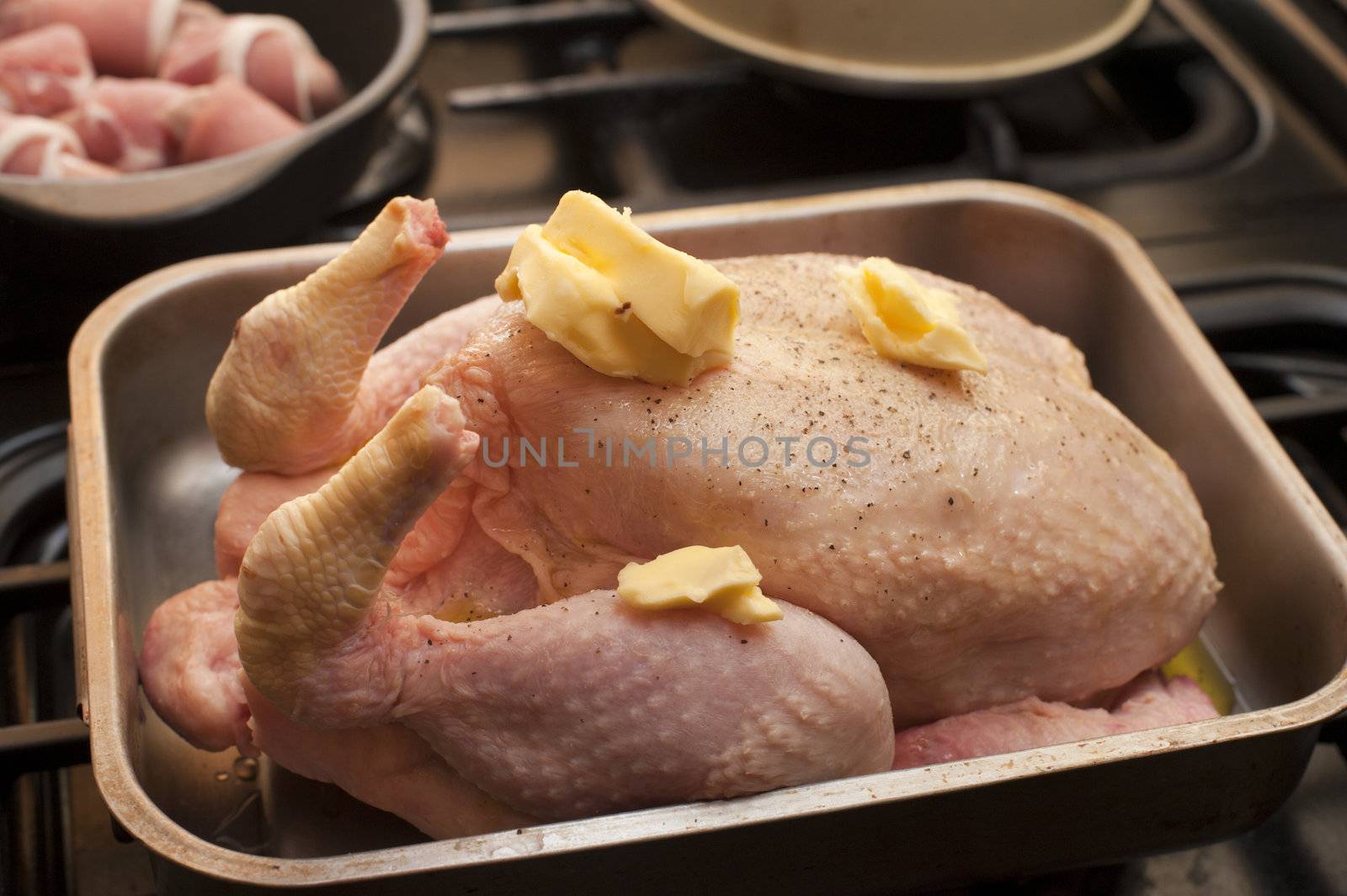 Cooking a roast turkey with the uncooked bird in a roasting pan garnished with dollops of butter ready to be placed in the oven