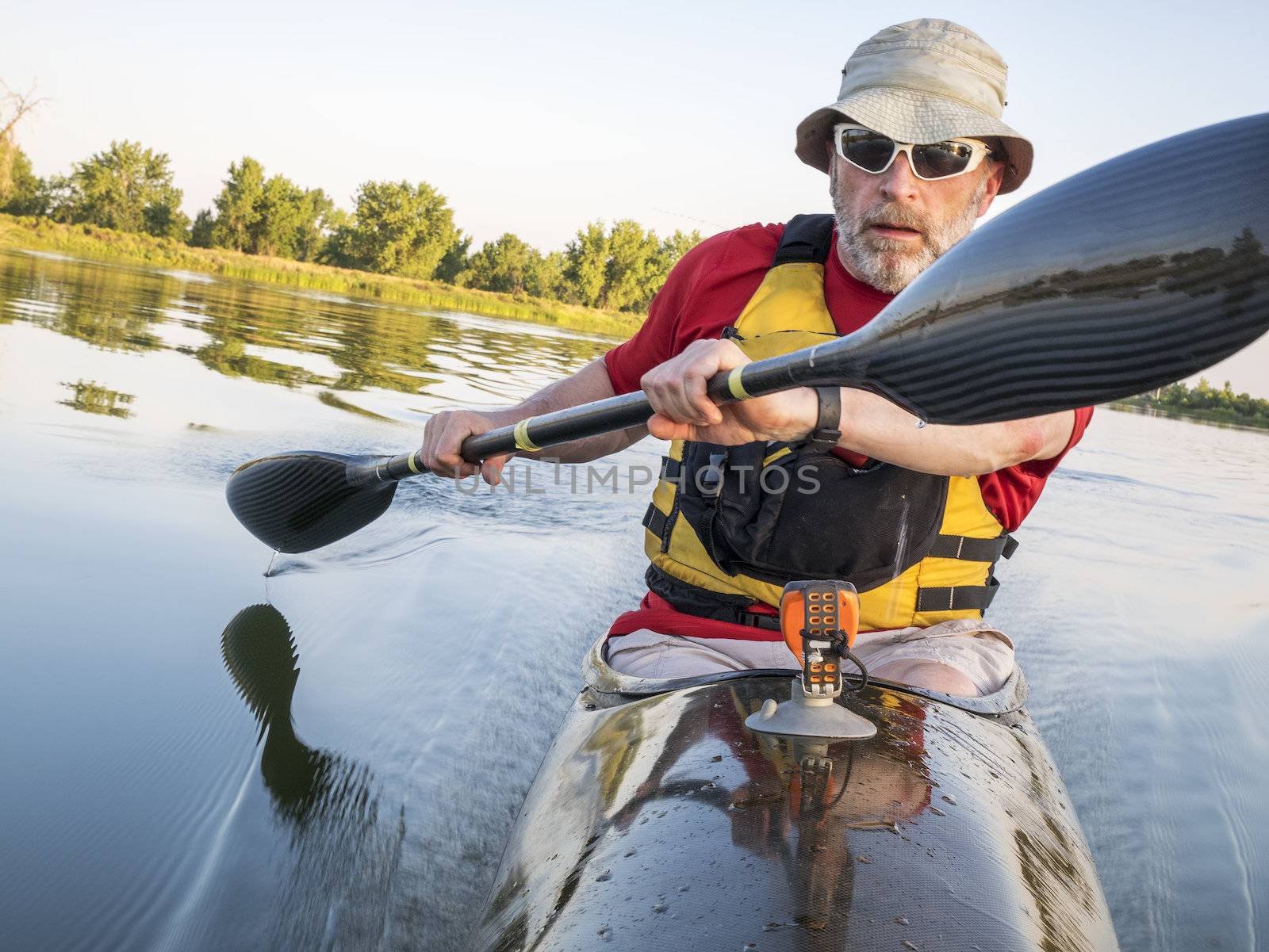 senior male is paddling a fast racing sea kayak  with a wing paddle on a calm lake, Fort Collins, Colorado
