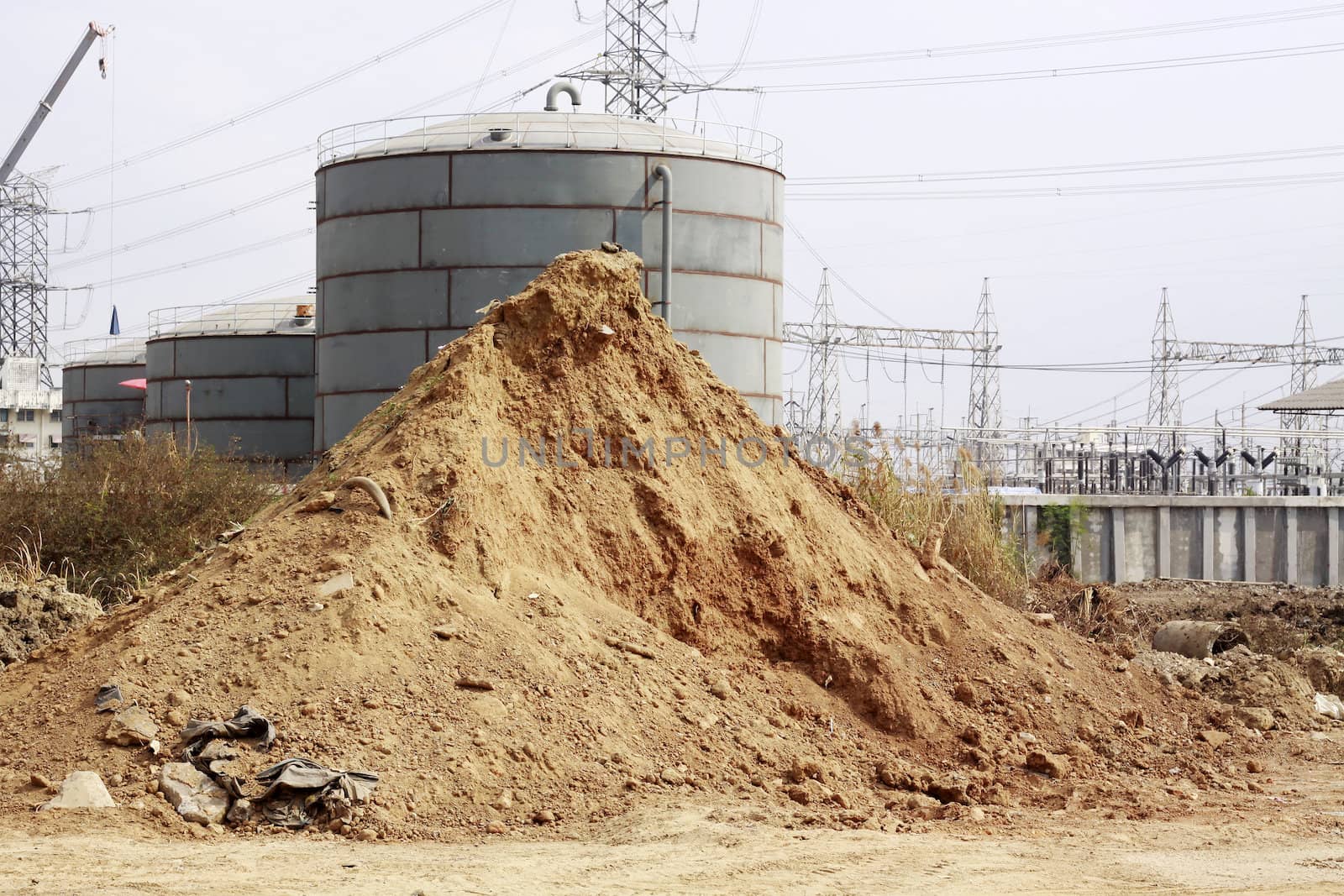 Pile of dry soil and sand in front of big Industrial tanks 