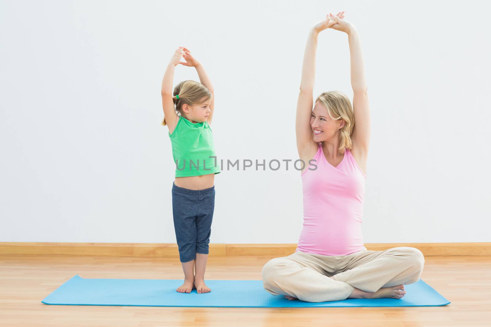 Pregnant smiling mother and daughter doing yoga together in a fitness studio