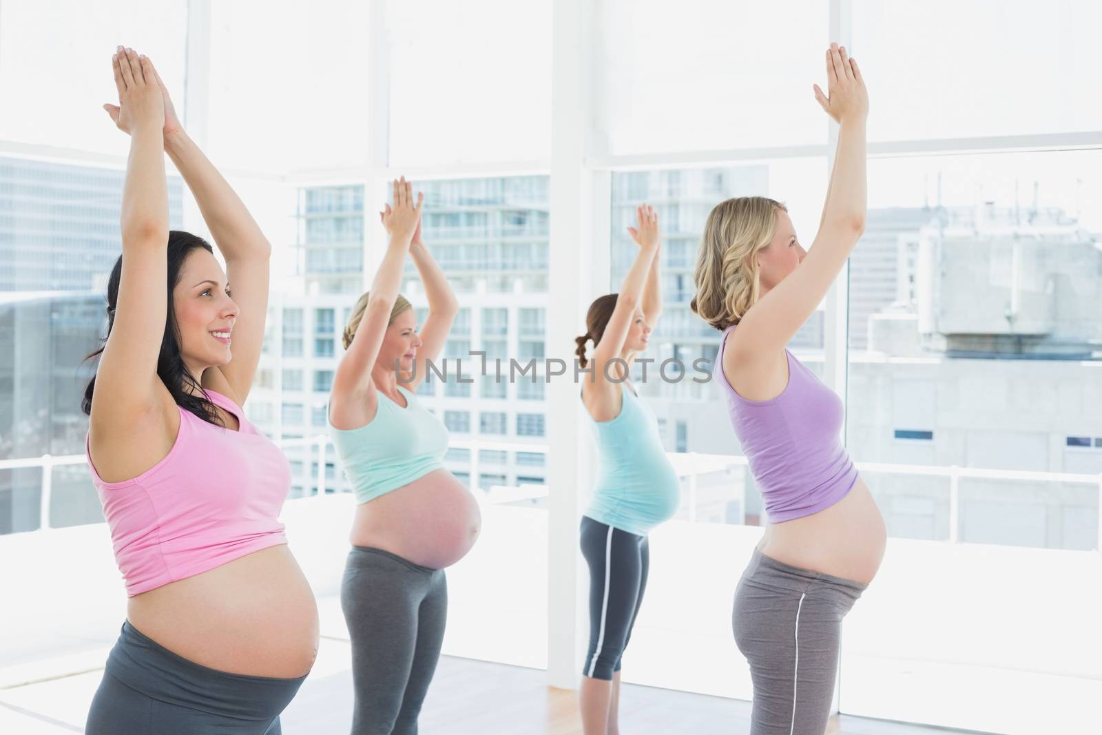 Happy pregnant women in yoga class standing in tree pose in a fitness studio
