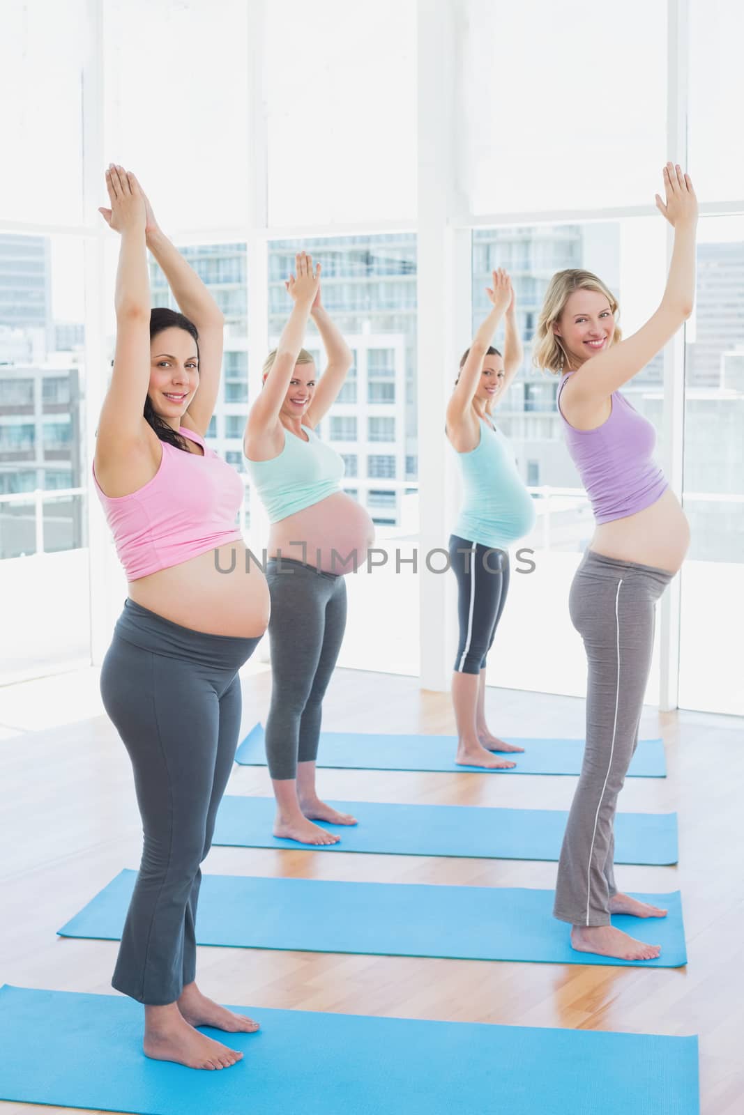 Smiling pregnant women in yoga class standing in tree pose looking at camera in a fitness studio