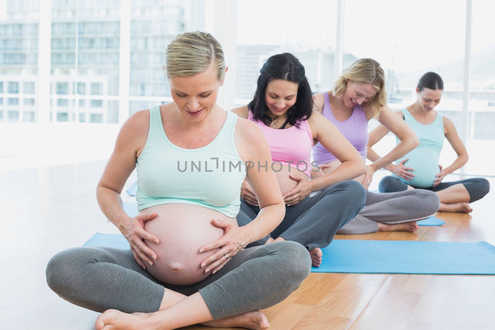 Pregnant women sitting on mats touching their bumps in a fitness studio