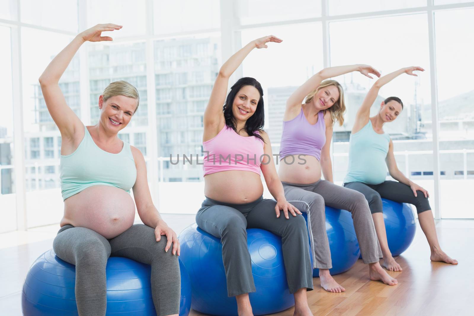Pregnant women sitting on exercise balls stretching arms in a fitness studio