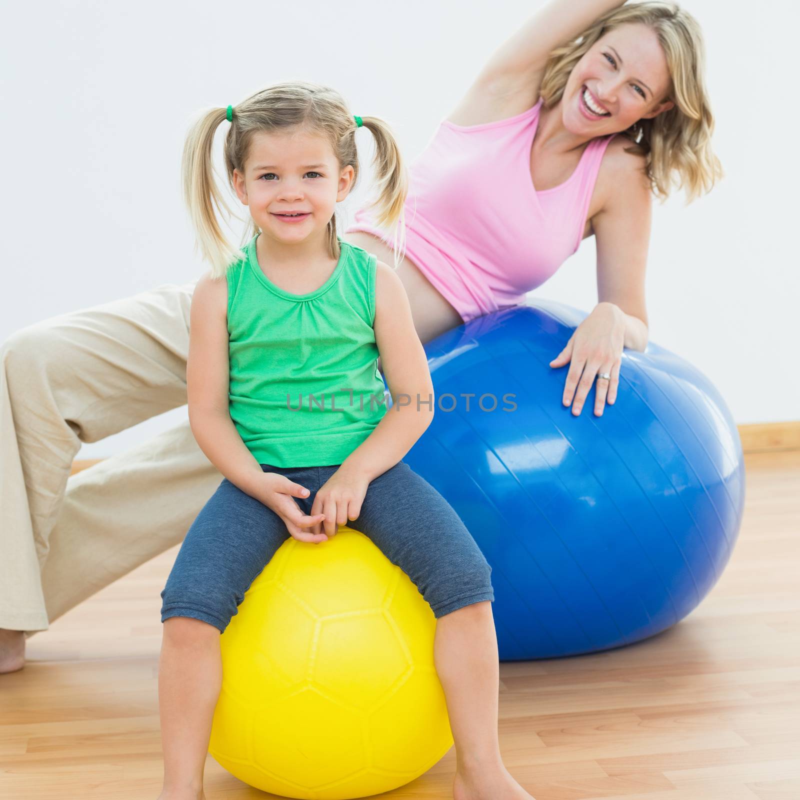 Smiling pregnant woman exercising on exercise ball with young daughter by Wavebreakmedia