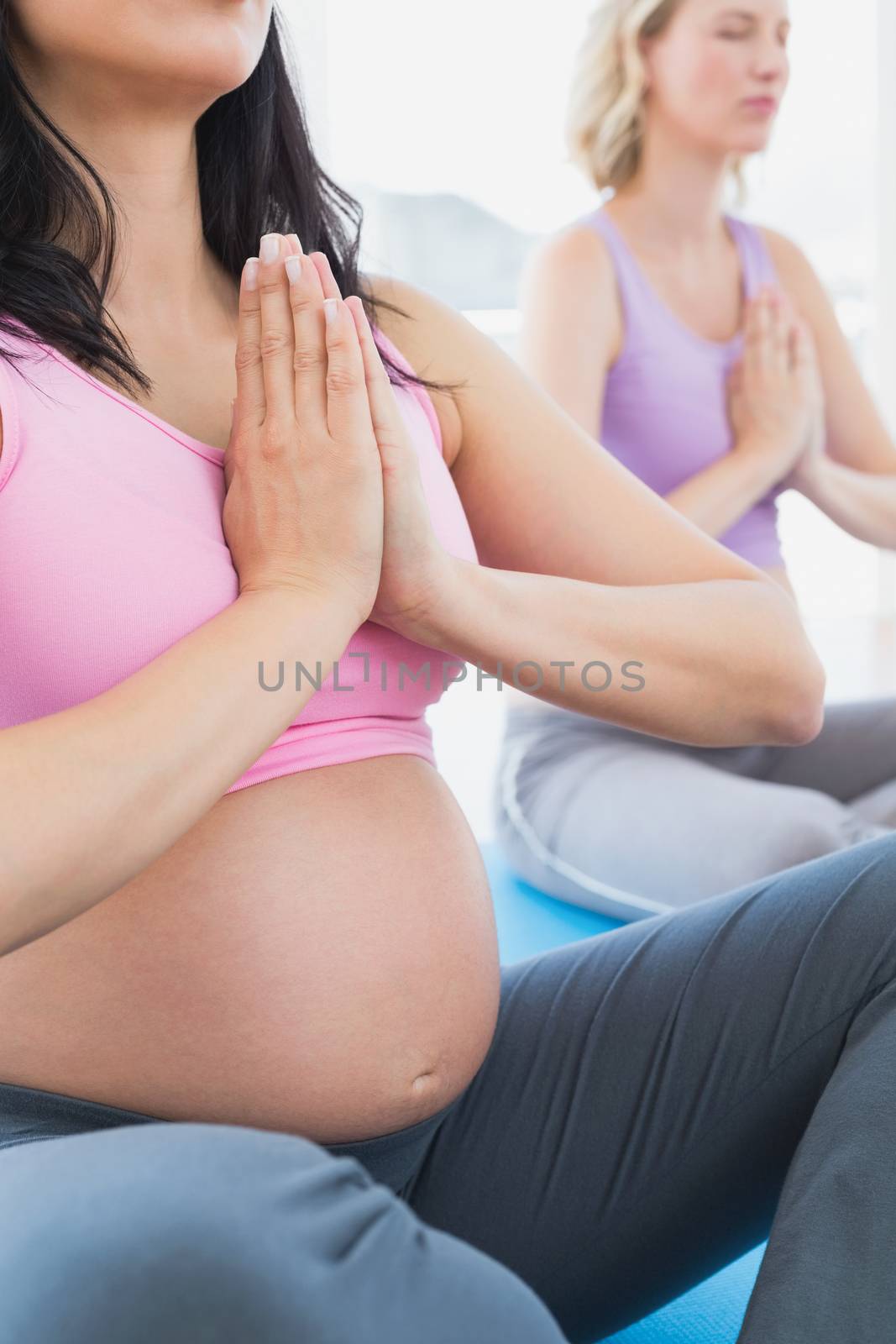 Meditating pregnant women at yoga class with hands together in a fitness studio