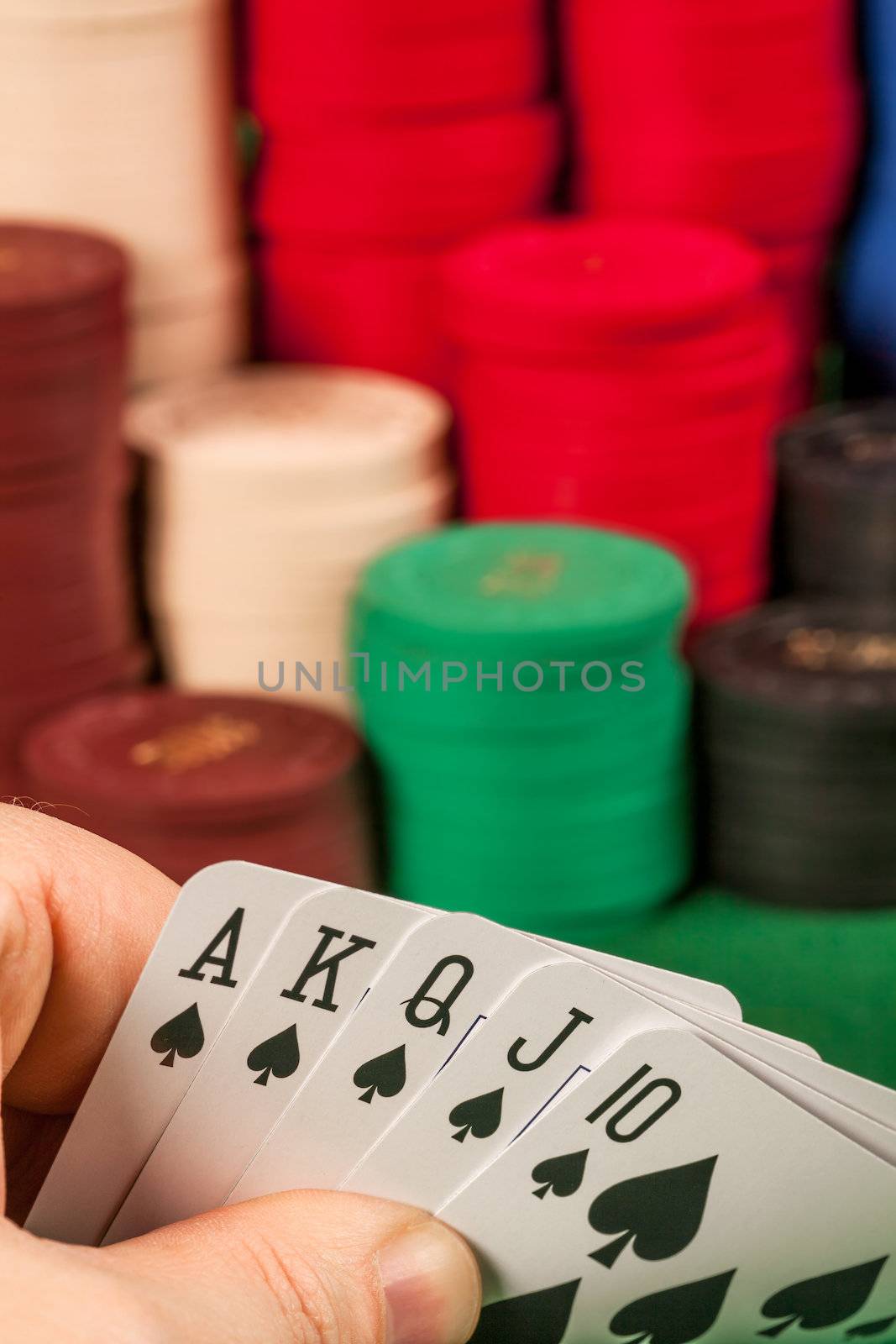 Photo of a person holding a royal flush in front of stacks of gambling chips.
