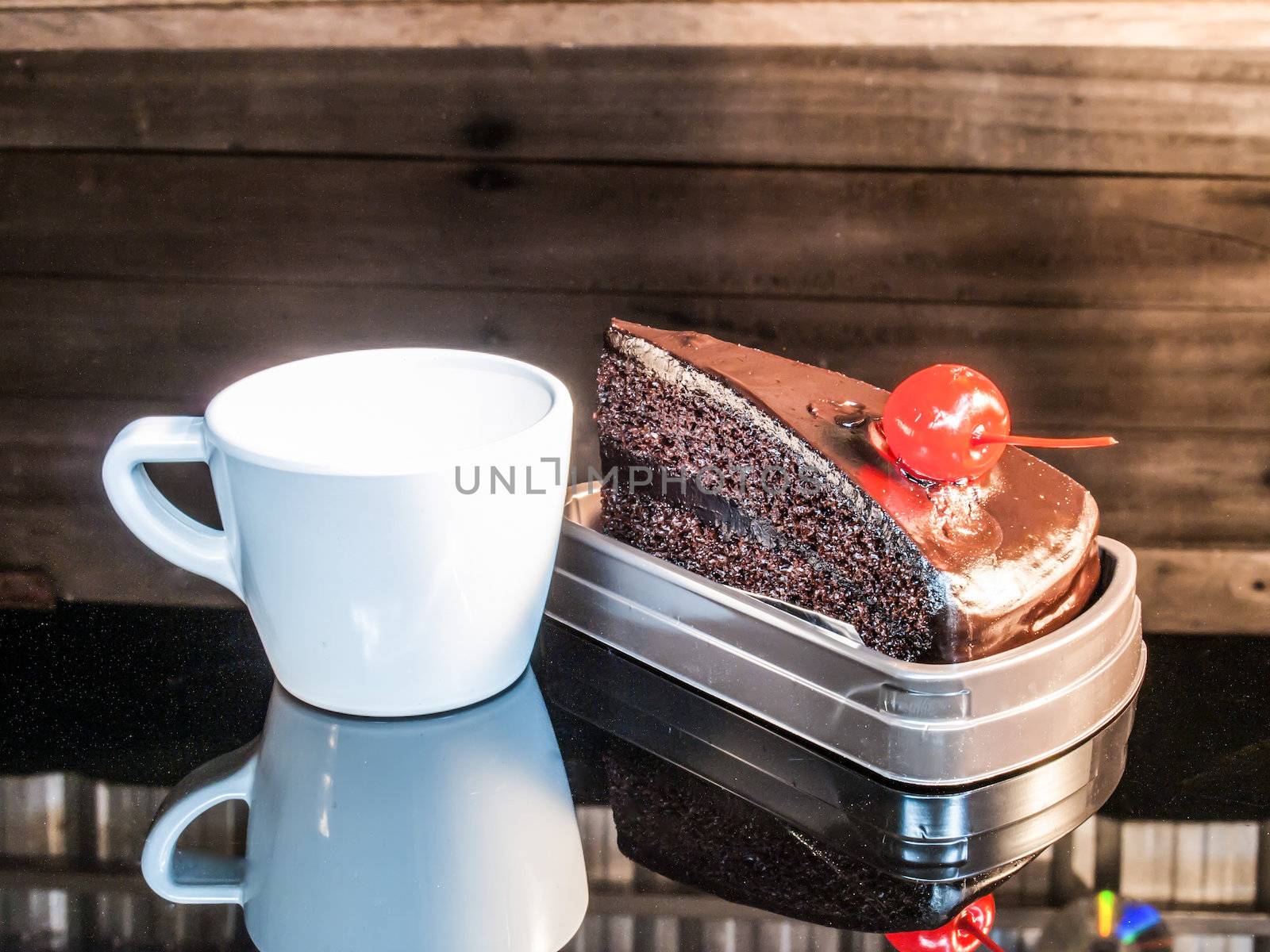 Chocolate Cake and white cup on black glass on wood background.