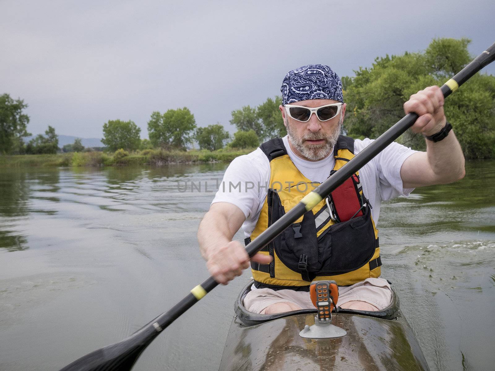 senior male paddler training in a narrow fast racing kayak on a lake, focus on paddler's face