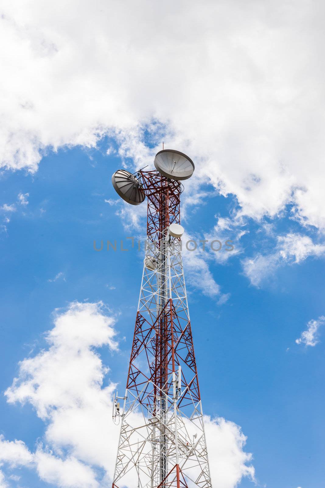 Red and white tower of communications with a lot of different antennas under clear sky.