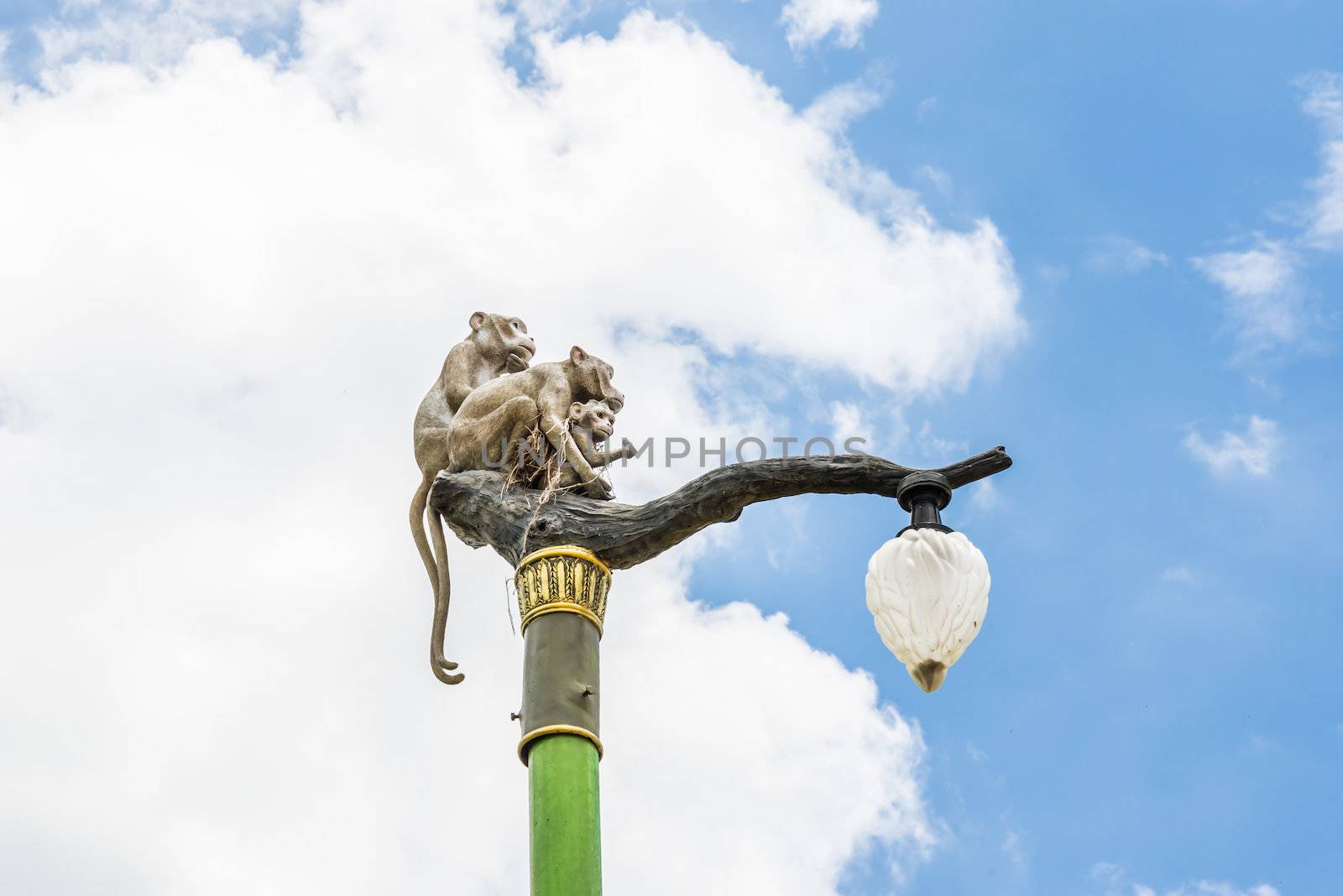 Statue of a monkey family on lamp post on blue sky and clouds.