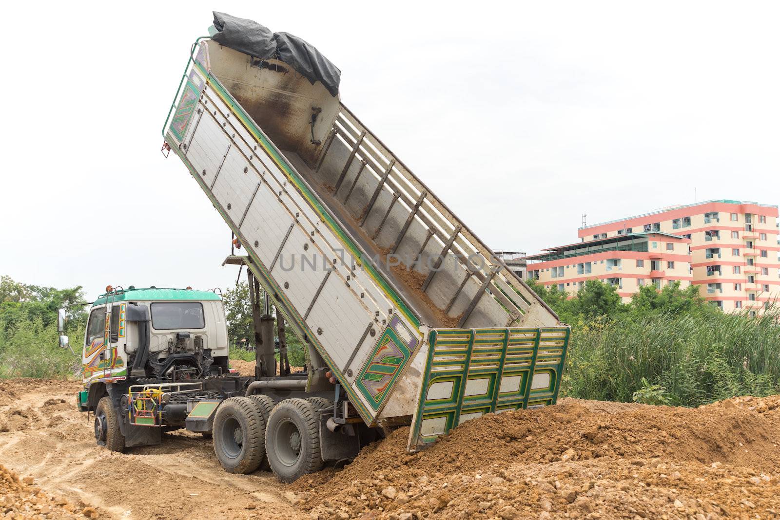 Dump truck dumps its load of rock and soil on land by iamway