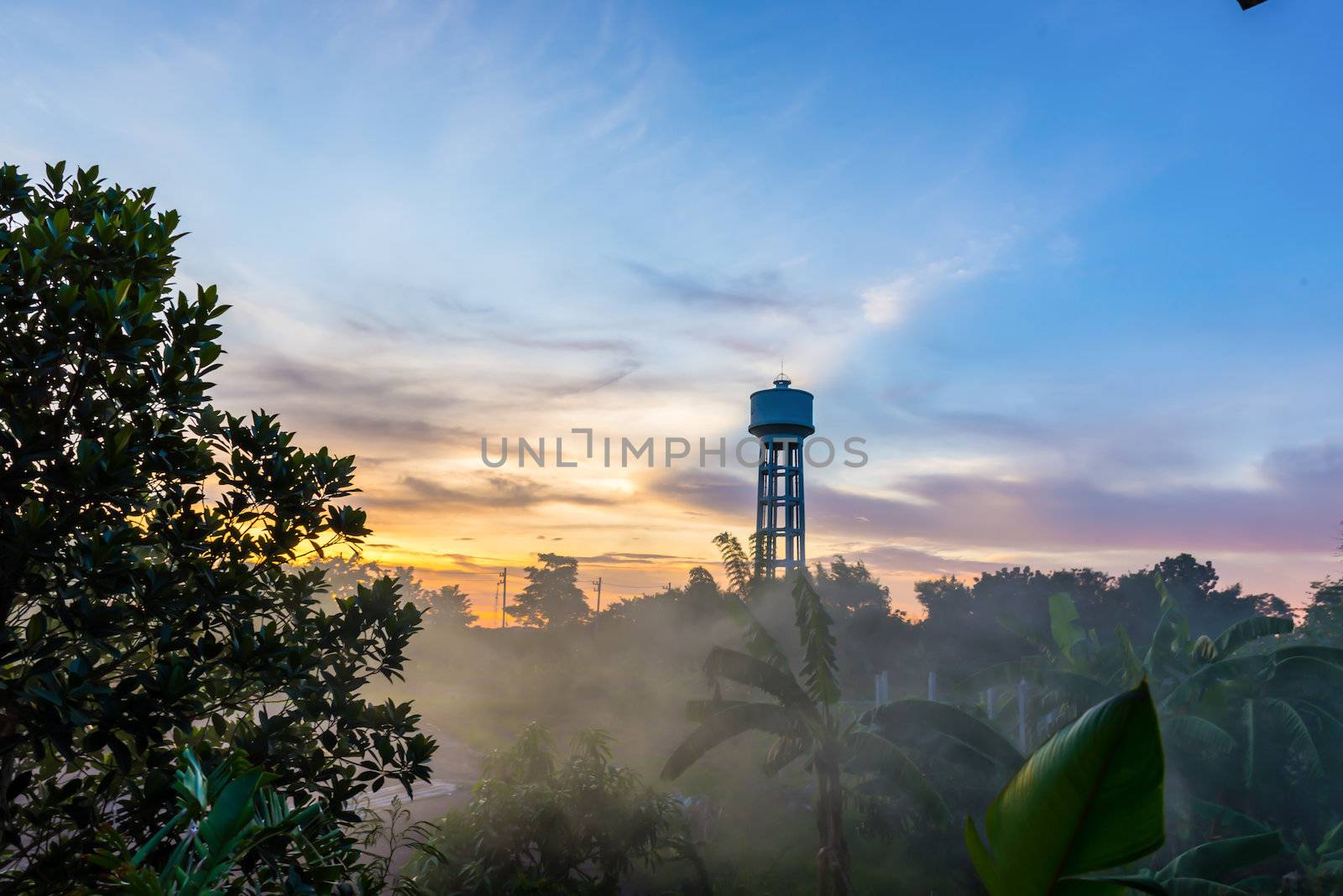 Water tower painted white on sunset and haze.