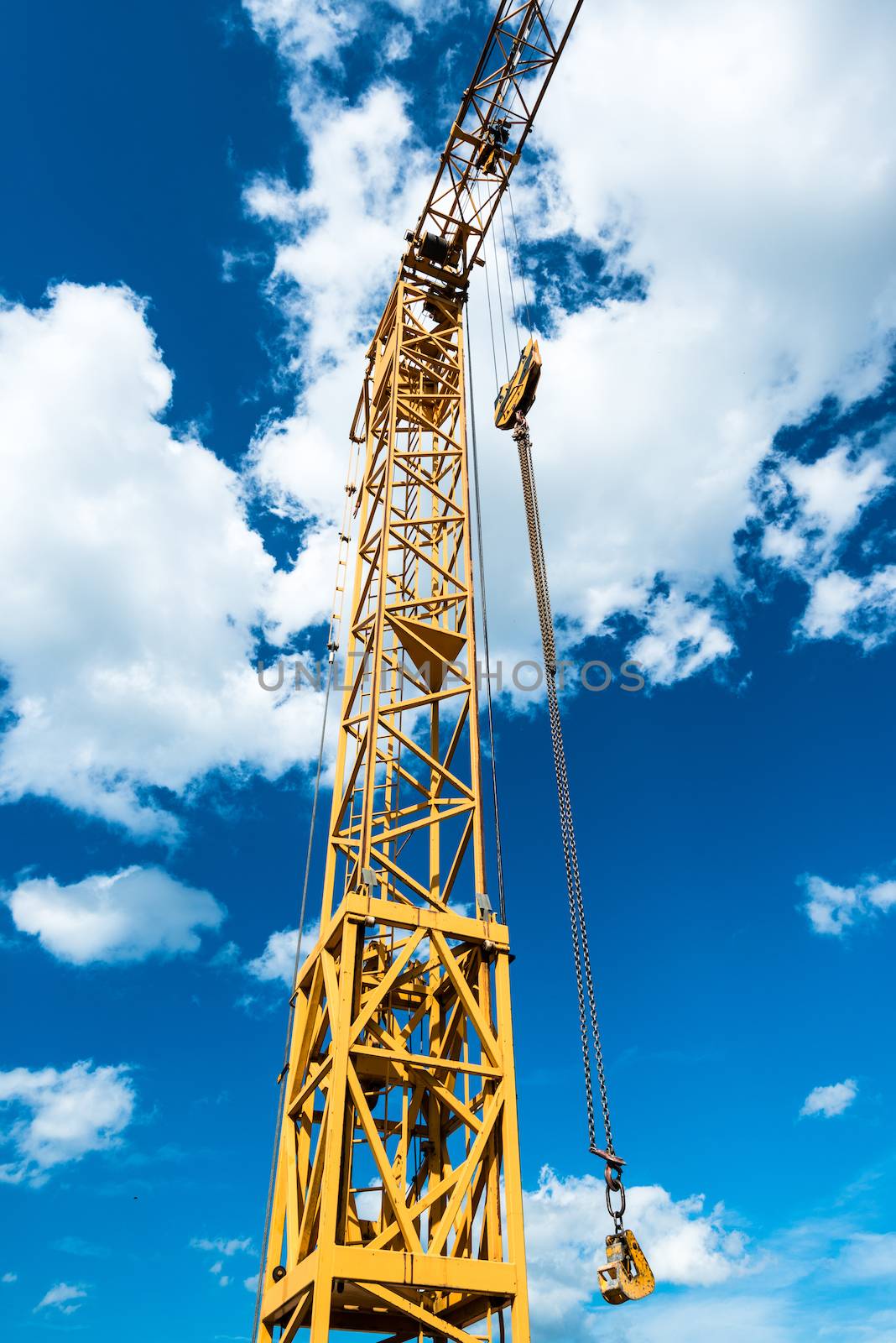 Yellow construction crane detail against great blue cloudy sky