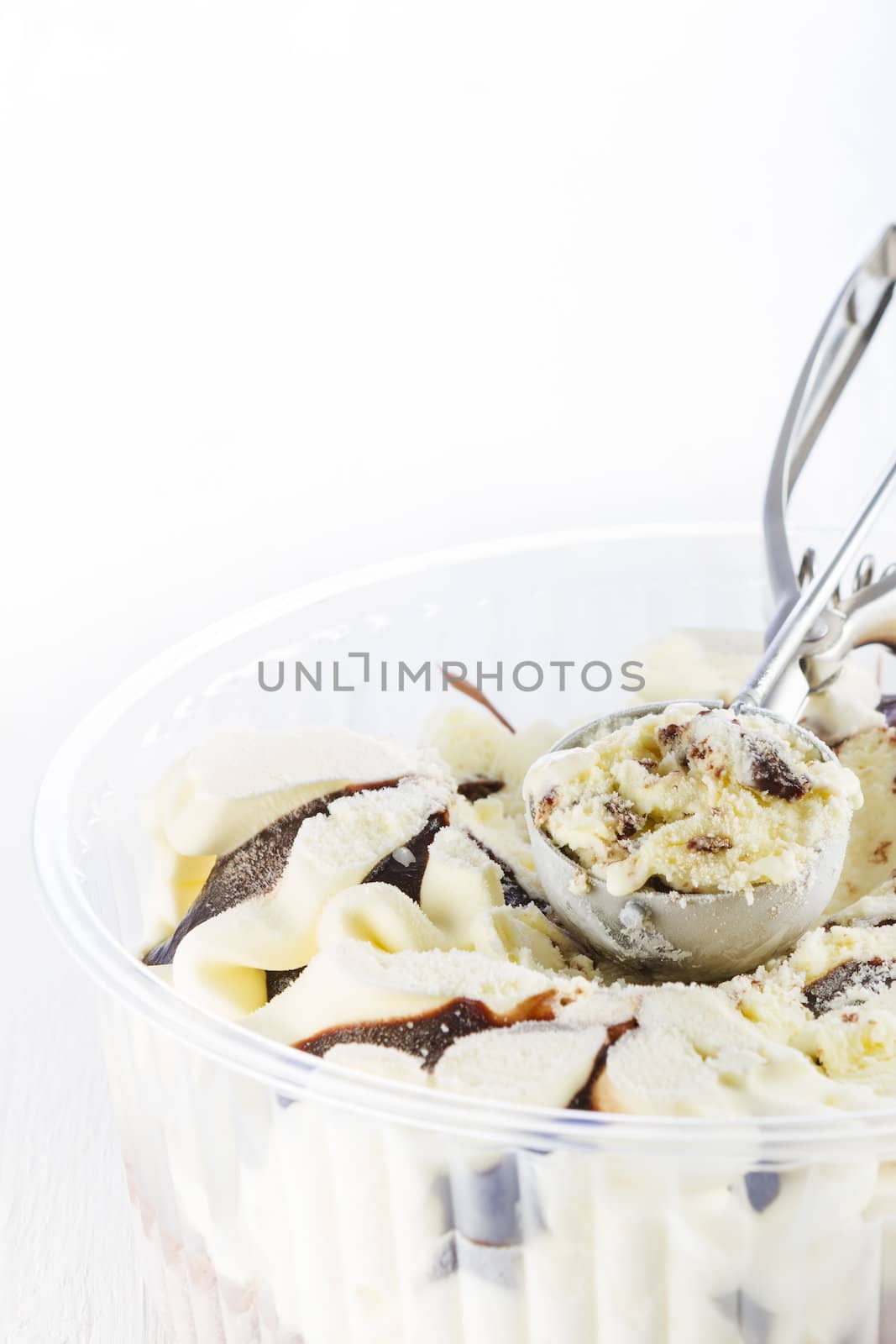 Vanilla with chocolate ice cream scoop scooped out of a container on white wooden background