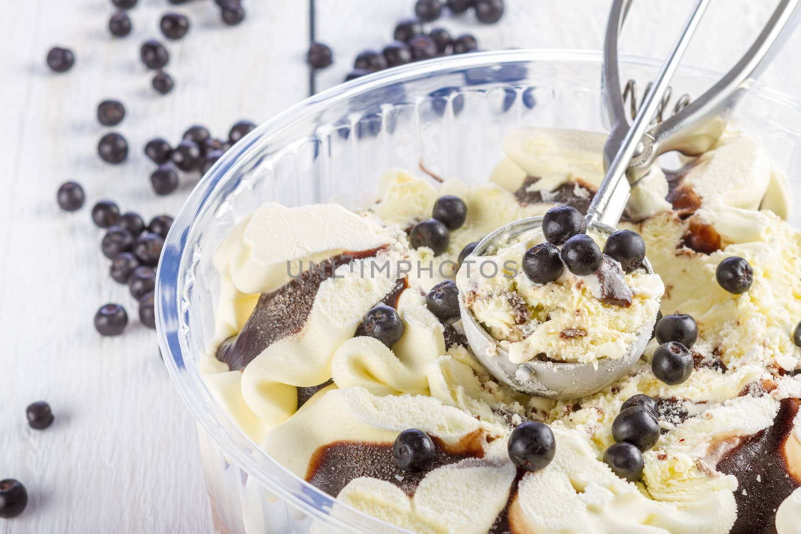 vanilla and chocolate ice cream with blackberries scoop scooped out of a container on white wooden background