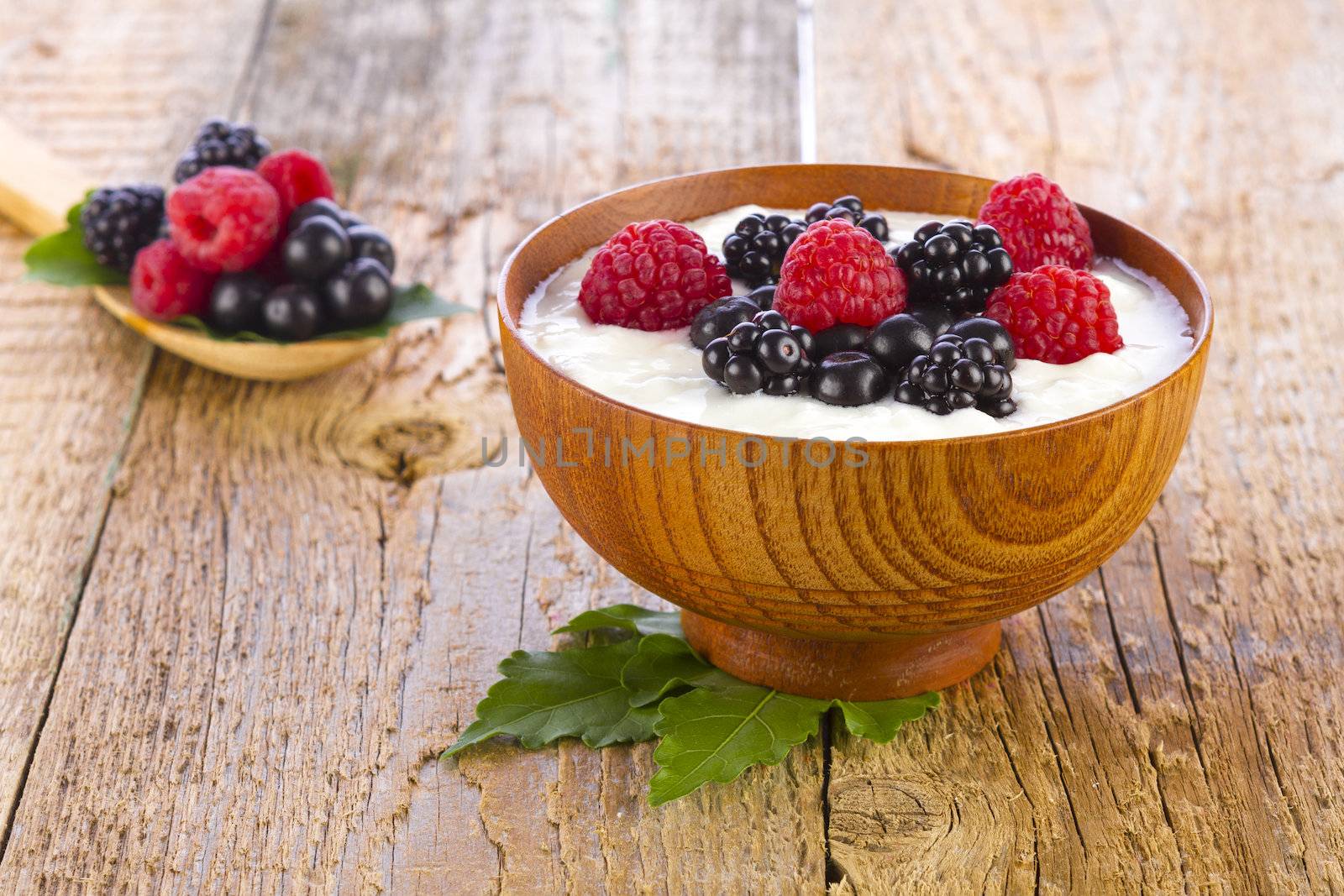 yogurt with wild berries in wooden bowl on wooden background