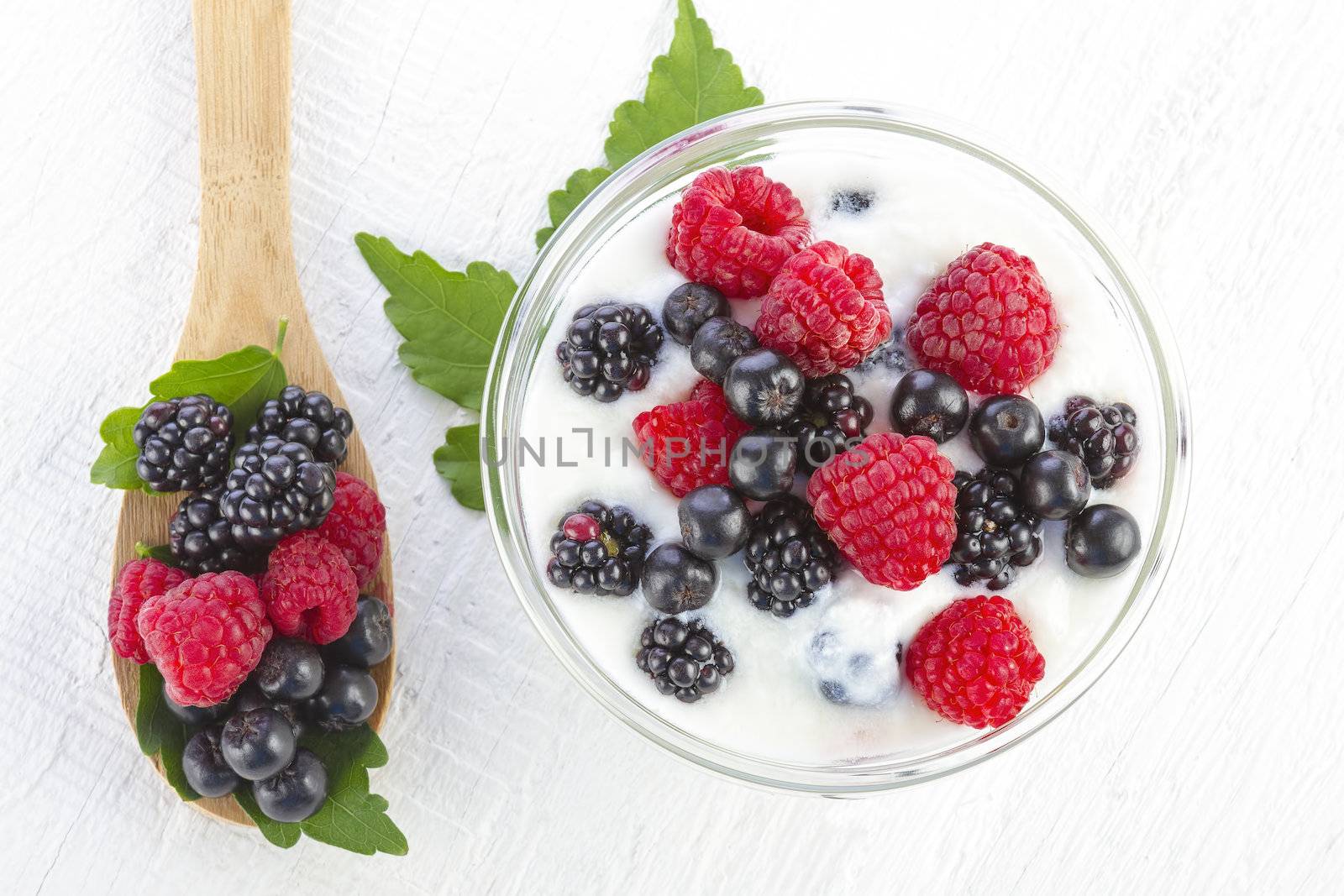 Yogurt with forest berries in bowl on white wooden background