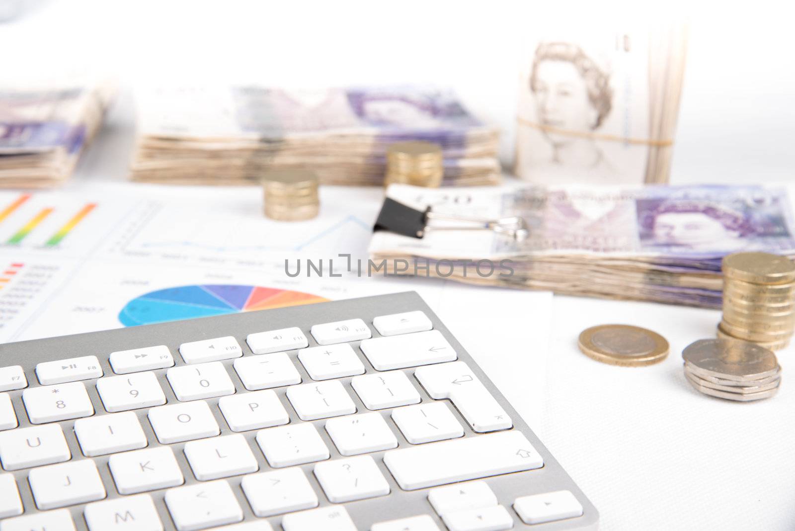 British pound sterling coins and bank notes on desk with keyboard and financial chart