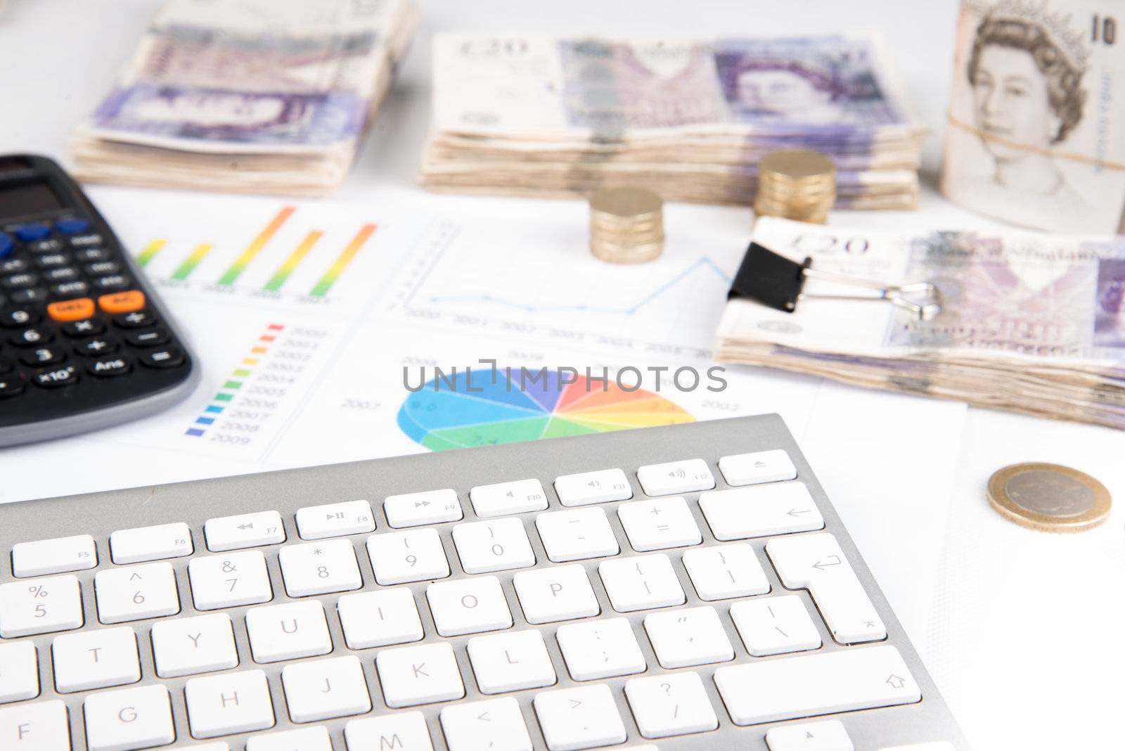 British pound sterling coins and bank notes on desk with keyboard and financial chart