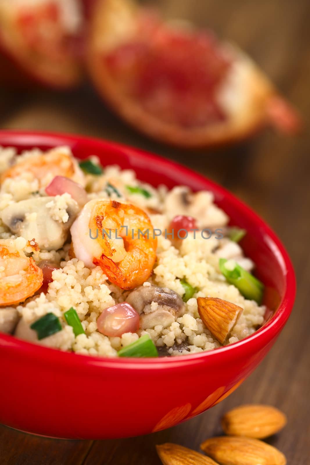 Couscous dish with shrimps, mushroom, almond, pomegranate seeds and green onion served in red bowl (Selective Focus, Focus on the tail of the shrimp on the top of the meal) 