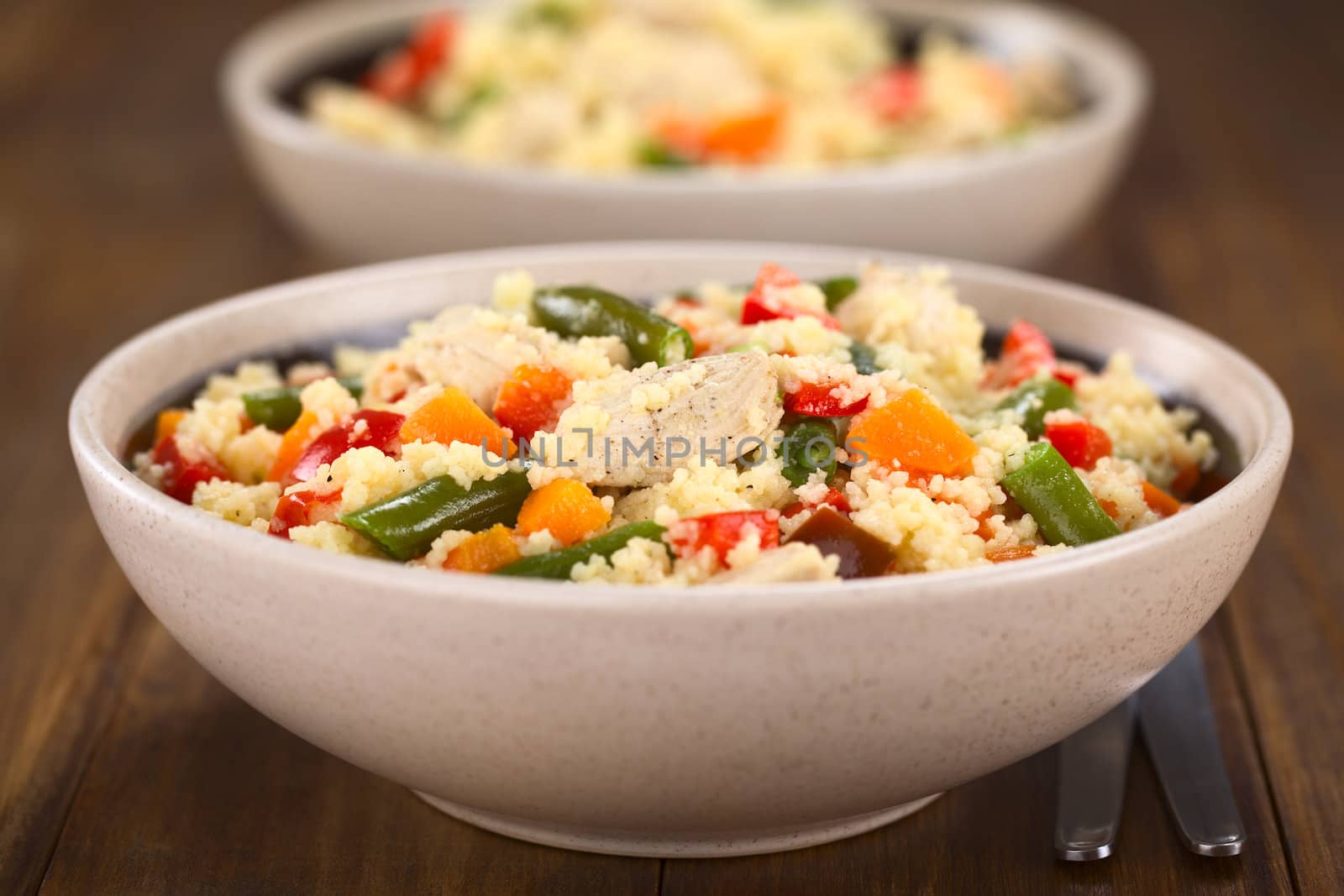 Two bowls of couscous dish with chicken, green bean, carrot and red bell pepper (Selective Focus, Focus on the chicken meat in the middle of the image) 