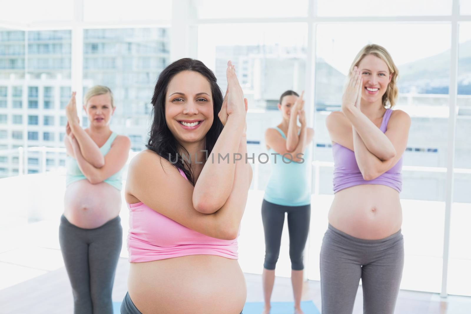 Happy pregnant women in yoga class standing in eagle pose in a fitness studio
