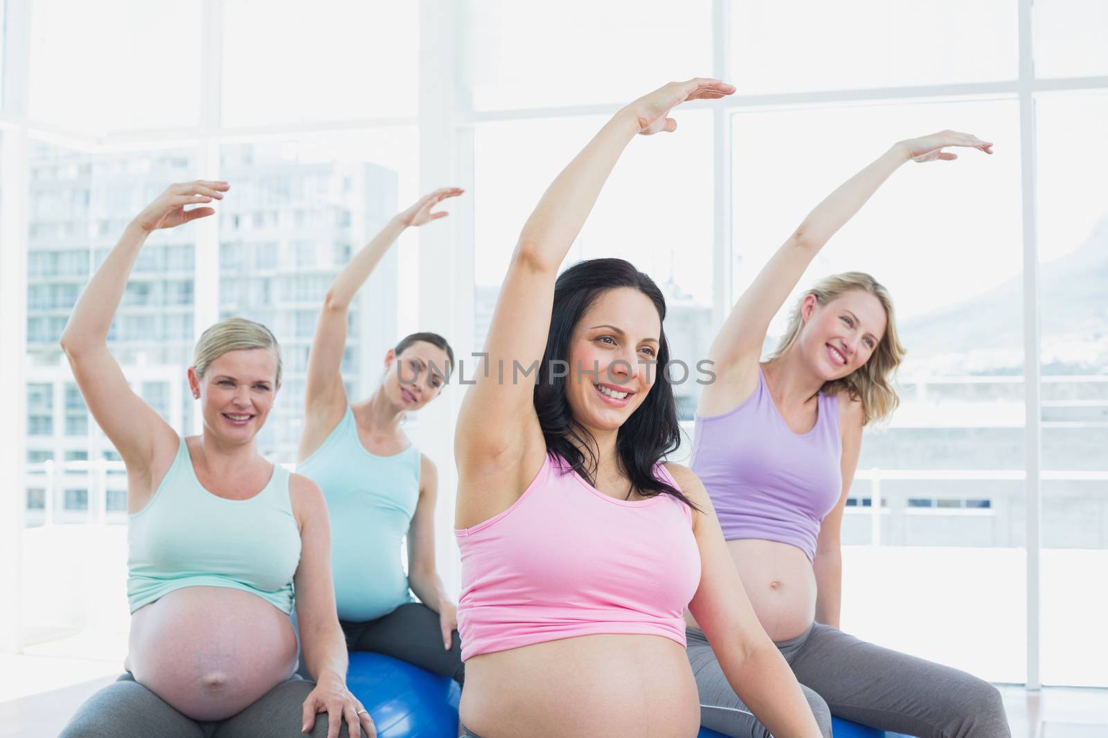 Happy pregnant women sitting on exercise balls stretching arms in a fitness studio