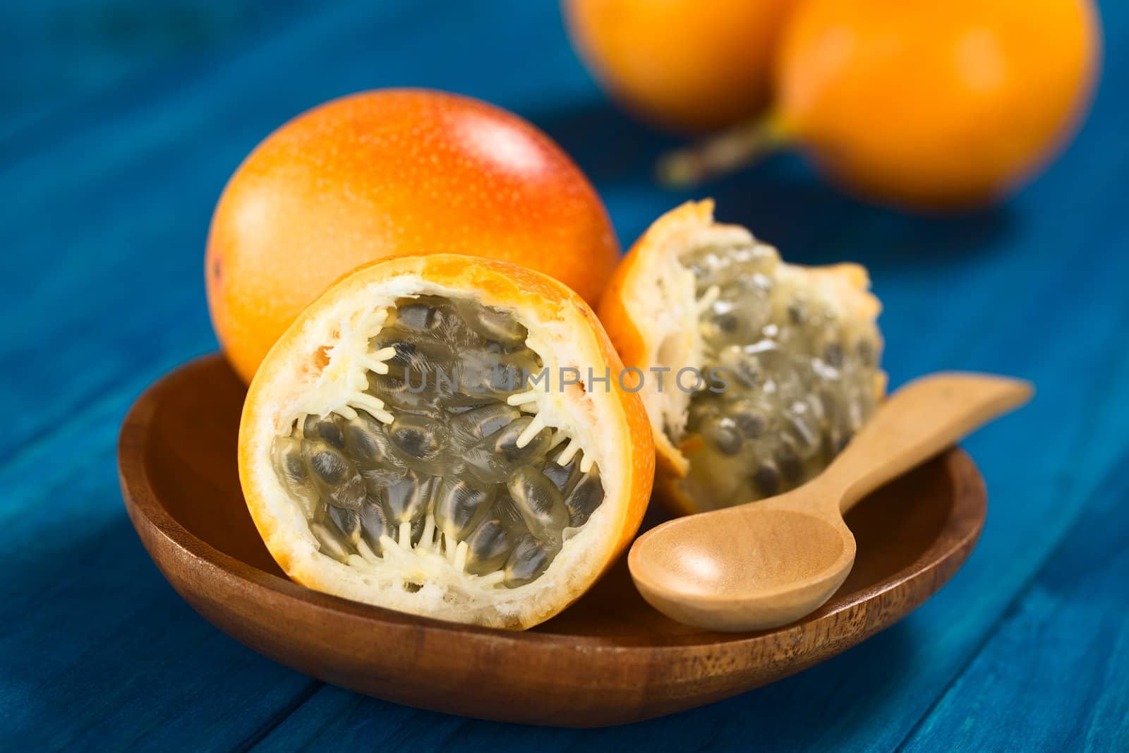 Sweet granadilla or grenadia (lat. Passiflora ligularis) fruit cut in half,  of which the seeds and the surrounding juicy pulp is eaten or is used to prepare juice, served on wooden plate with wooden spoon (Selective Focus, Focus on the front of the seeds)