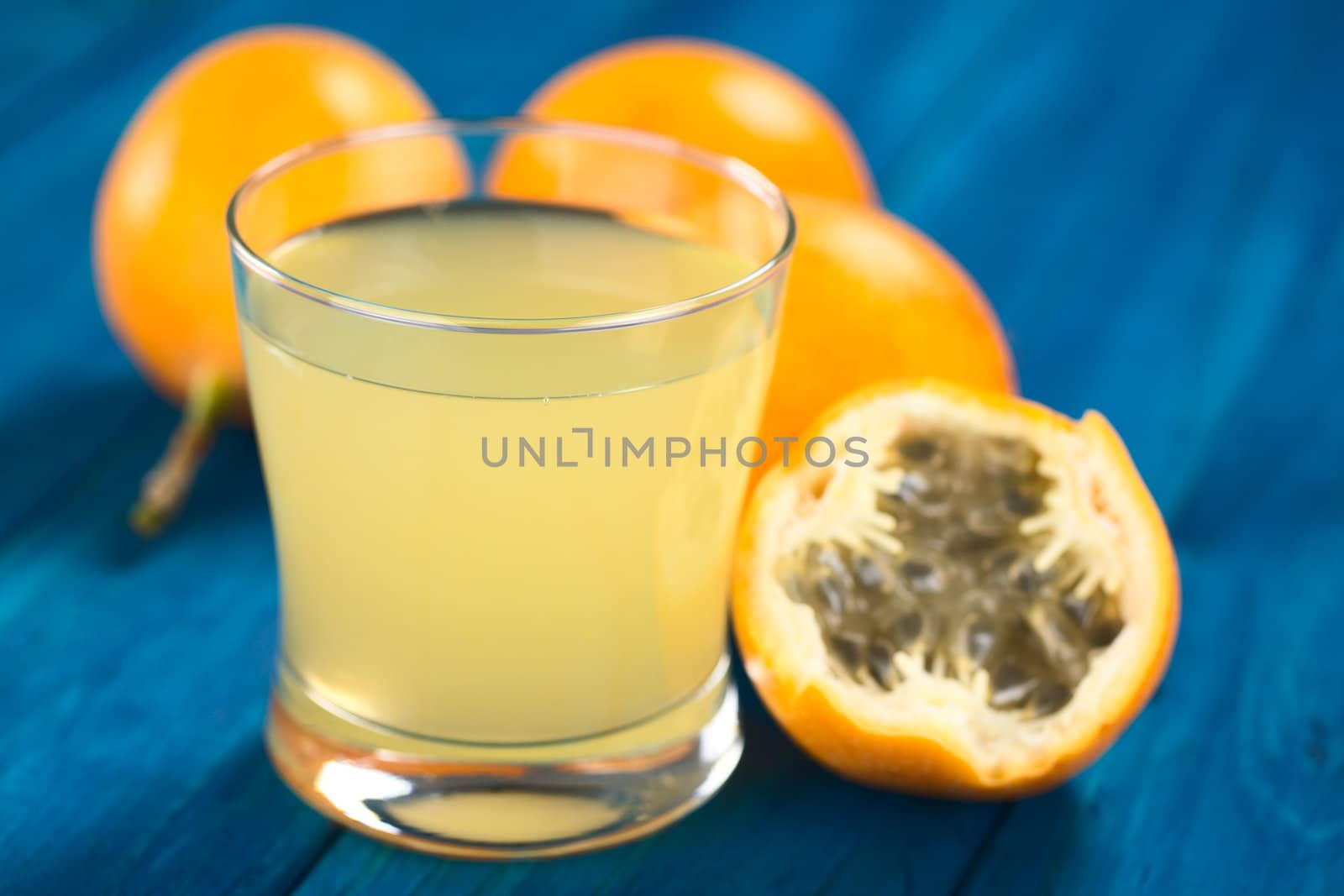 Fresh juice made of sweet granadilla or grenadia (lat. Passiflora ligularis) in glass with a half granadilla next to it (Selective Focus, Focus on the front rim of the glass)