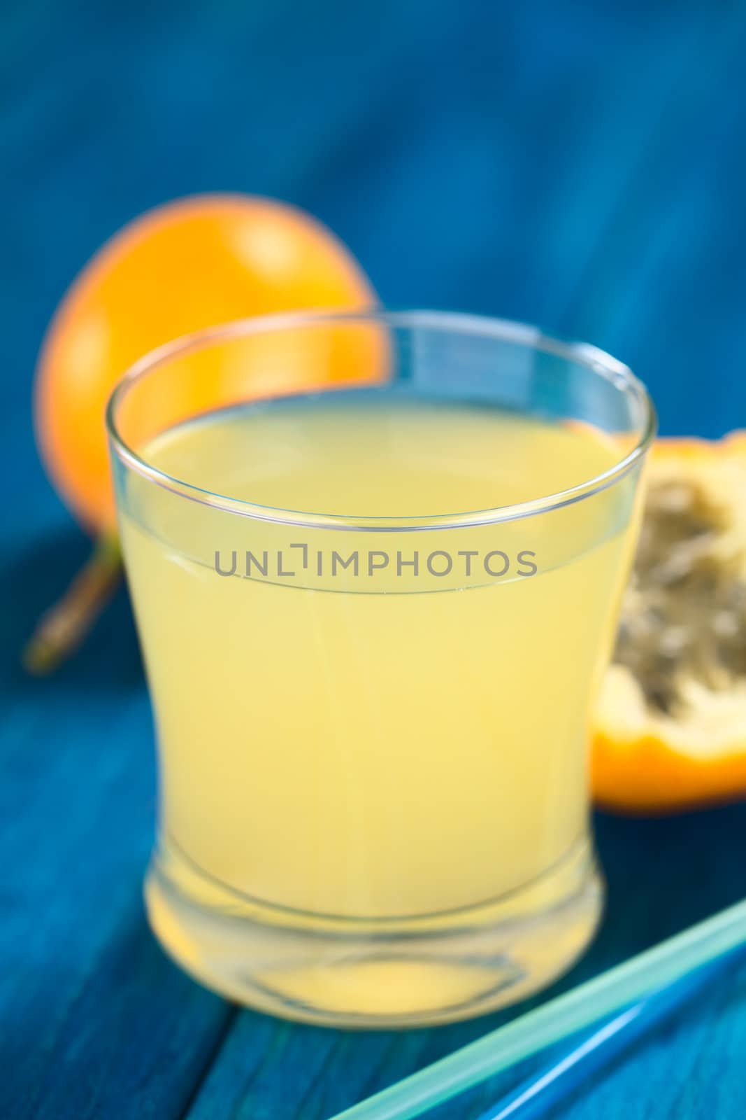 Fresh juice made of sweet granadilla or grenadia (lat. Passiflora ligularis) in glass with drinking straws in front (Selective Focus, Focus on the front rim of the glass)