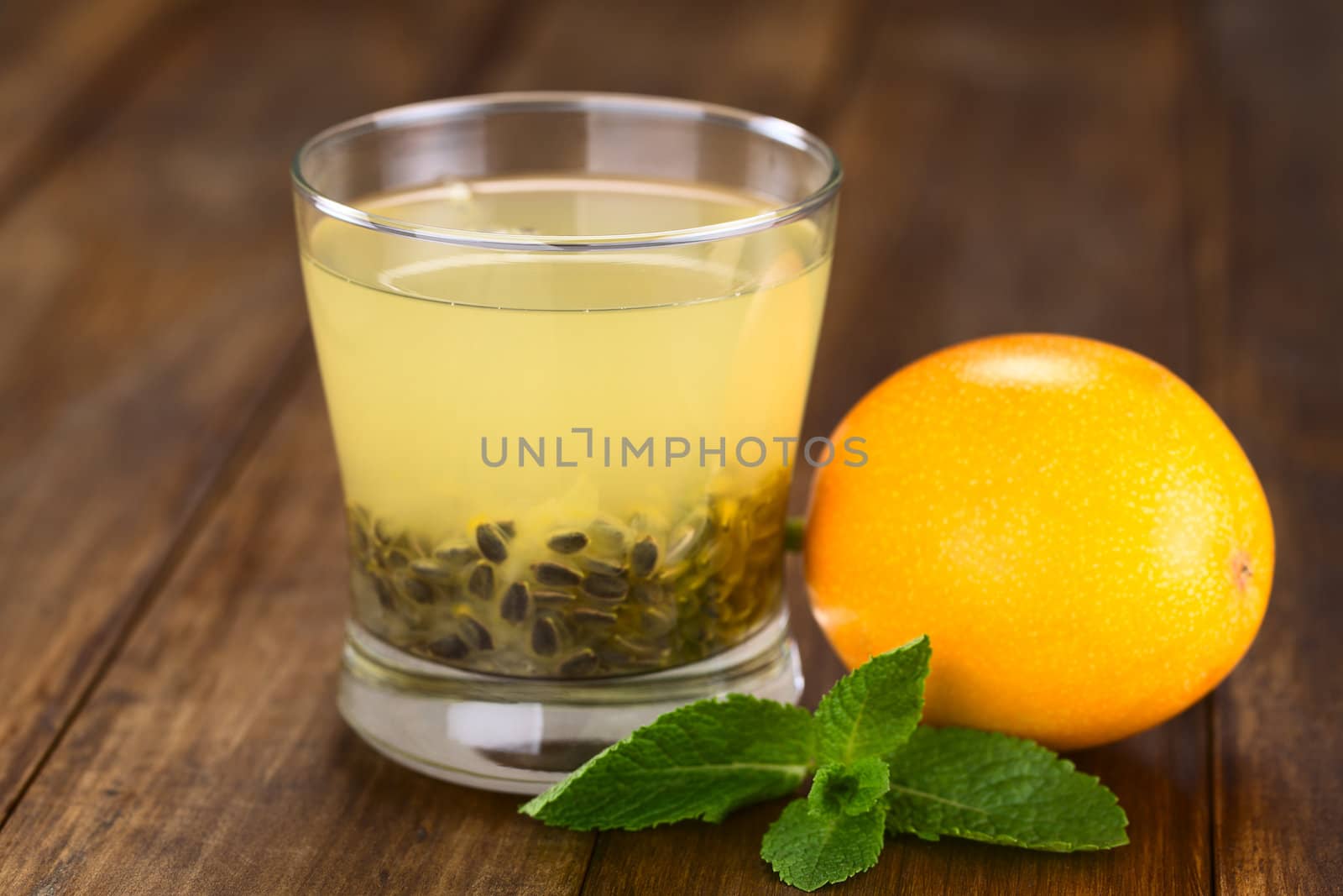 Fresh juice made of sweet granadilla or grenadia (lat. Passiflora ligularis) with its seeds in glass, granadilla fruit and mint leaf on the side (Selective Focus, Focus on the front rim of the glass)