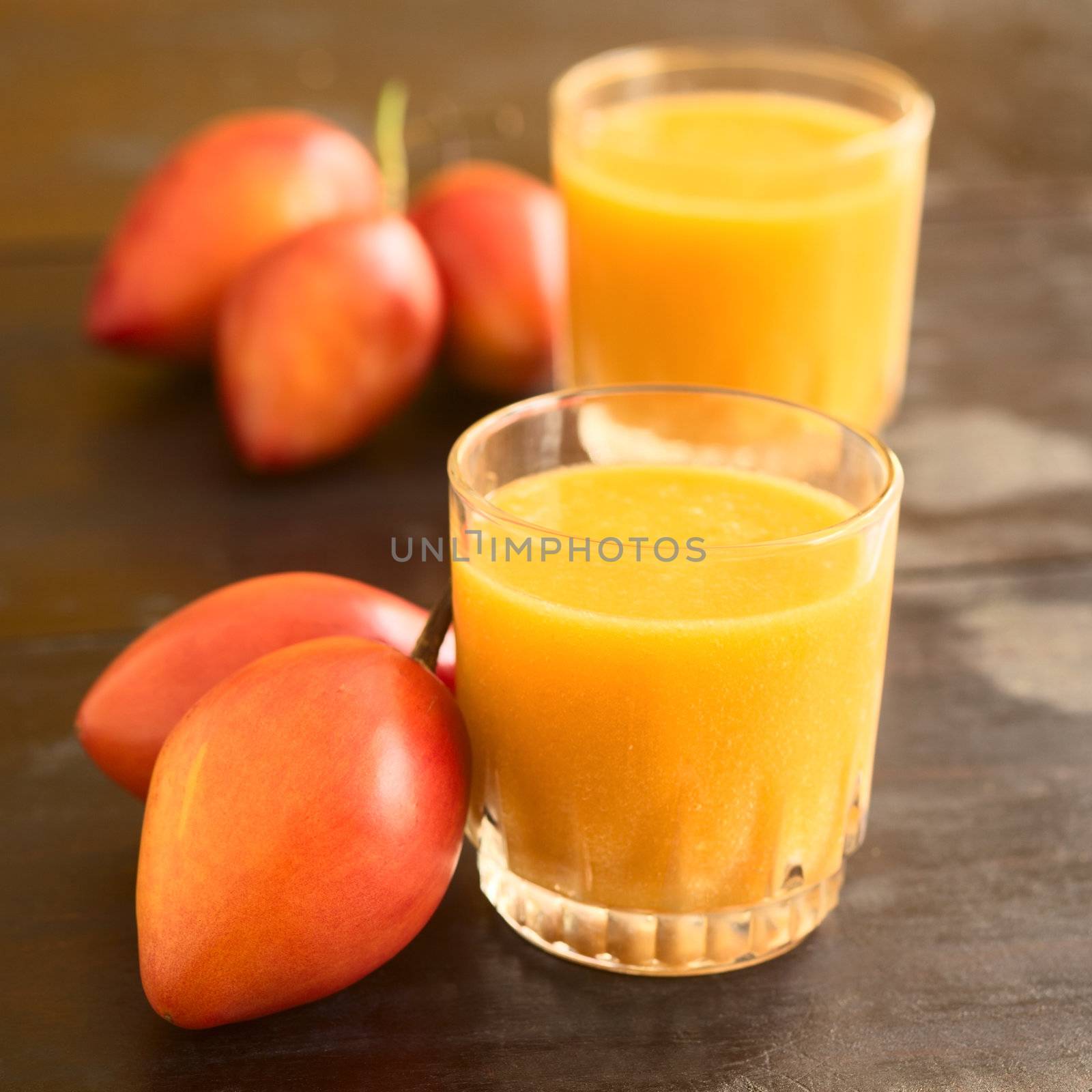 Freshly prepared tamarillo juice in glass with tamarillo (lat. Solanum betaceum) fruits beside (Selective Focus, Focus on the front rim of the glass)