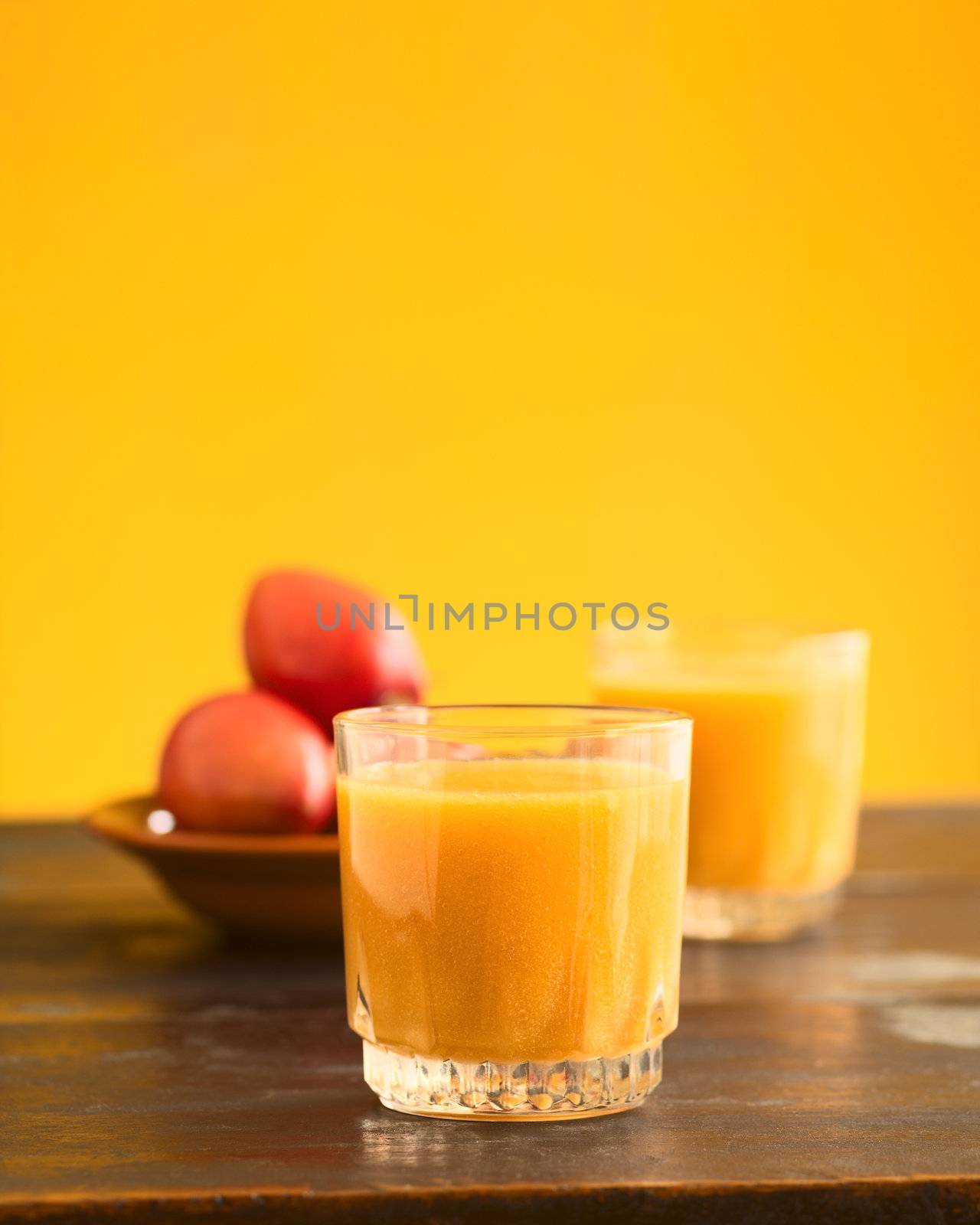 Freshly prepared tamarillo juice in glass with tamarillo (lat. Solanum betaceum) fruits in the back (Selective Focus, Focus on the front of the glass)
