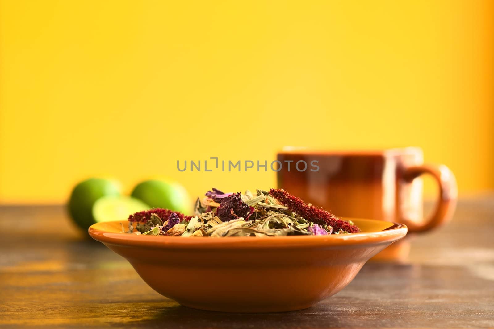 Horchata, a traditional Ecuadorian tea made of 28 different herbs in a bowl with a cup and limes in the back (Selective Focus, Focus on the top of the herbs)