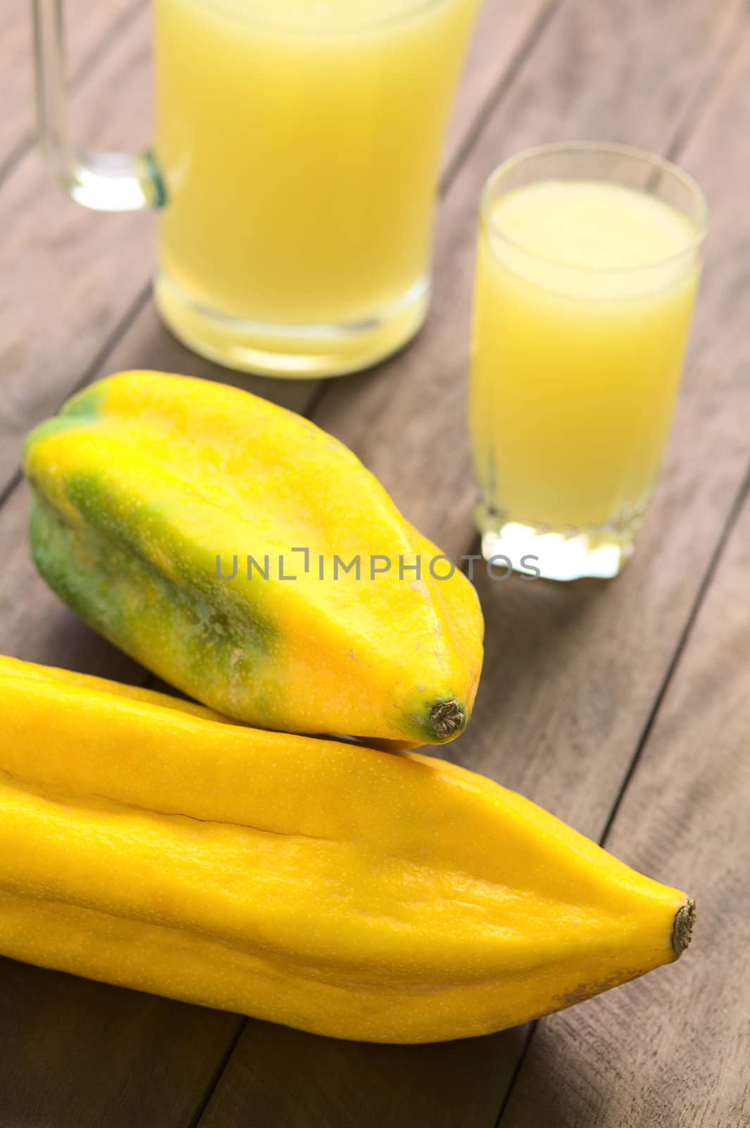 Two Ecuadorian Babaco fruits (lat. Vasconcellea x heilbornii; syn. Carica pentagona) with babaco juice in the back. Babaco is a fruit which is mainly used to prepare juices in Ecuador. (Selective Focus, Focus on the tip of the upper and the front of the lower fruit)