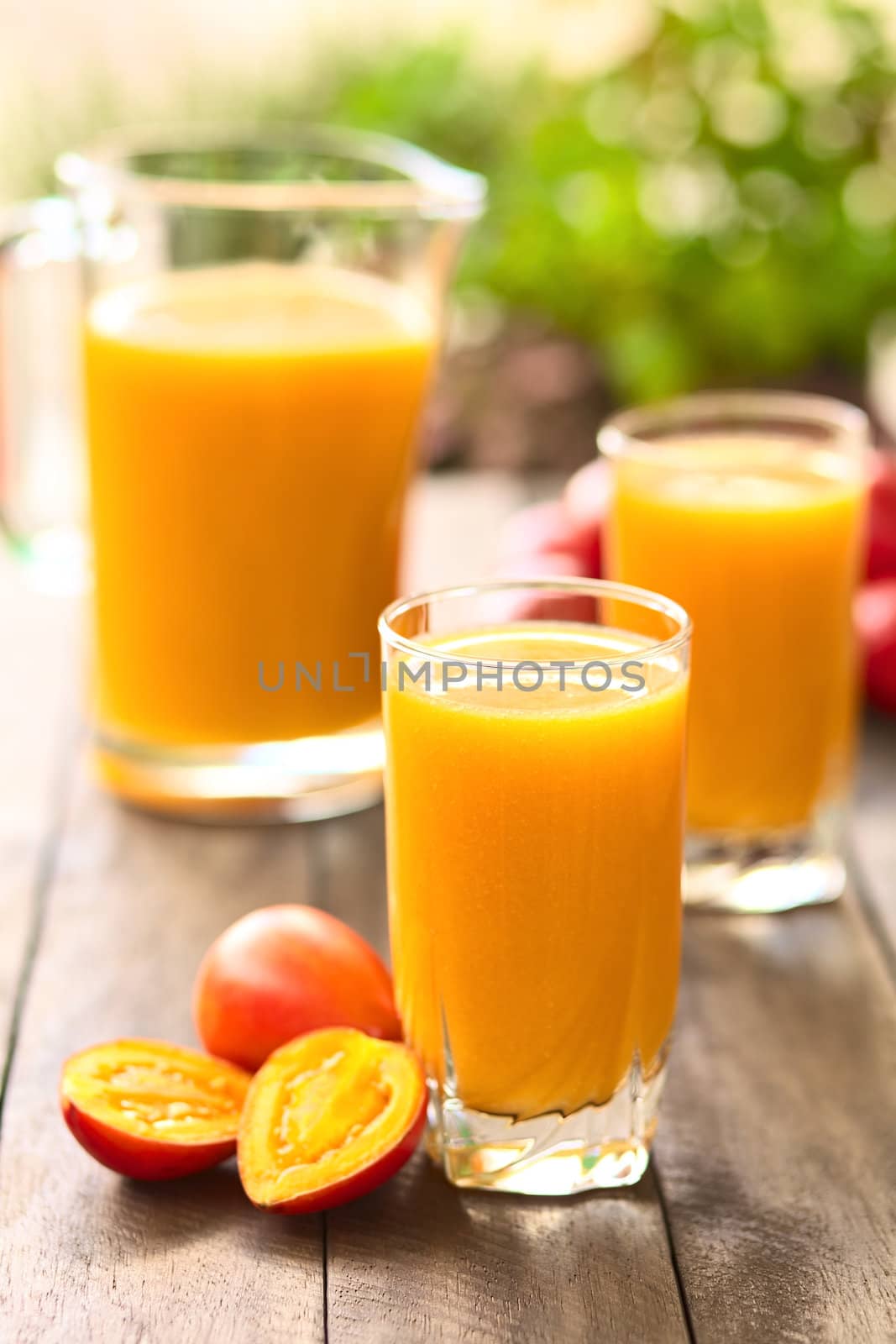 Fresh juice out of tamarillo fruits (lat. Solanum betaceum) on a table outdoors (Selective Focus, Focus on the front rim of the glass)