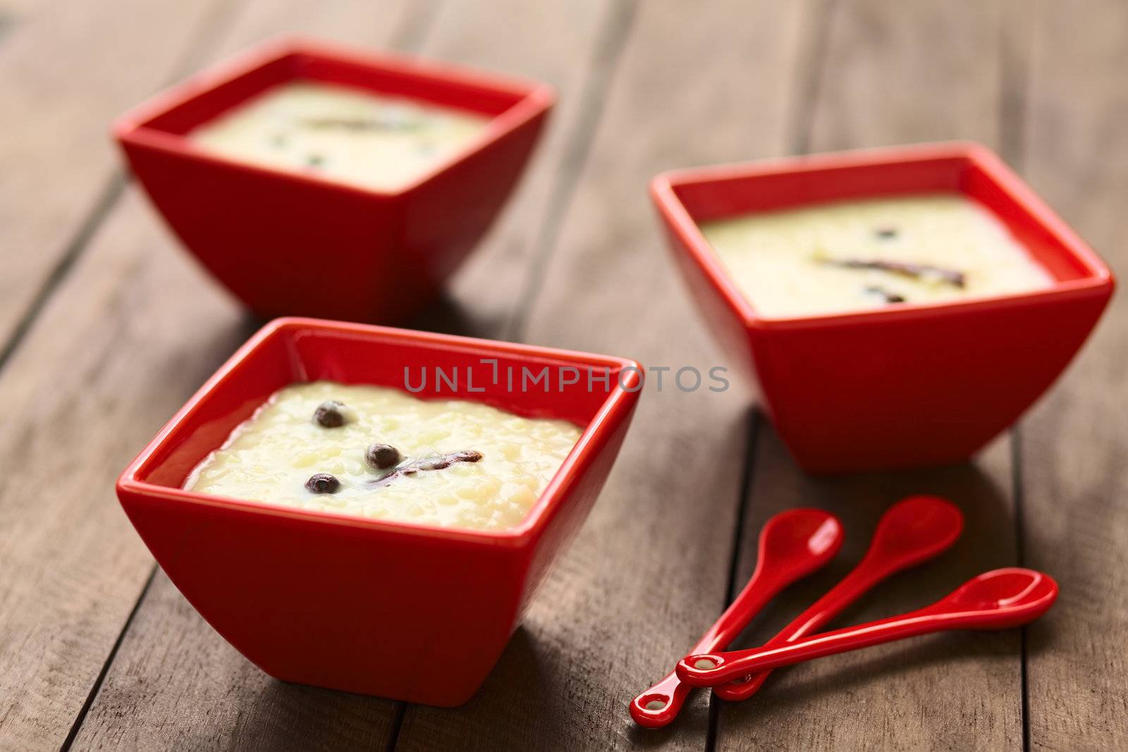 Three red bowls of the Ecuadorian dessert called morocho (coarsely ground white corn) cooked with milk, sugar and spices (cinnamon and allspice), similarly to rice pudding (Selective Focus, Focus on the middle of the lower morocho) 