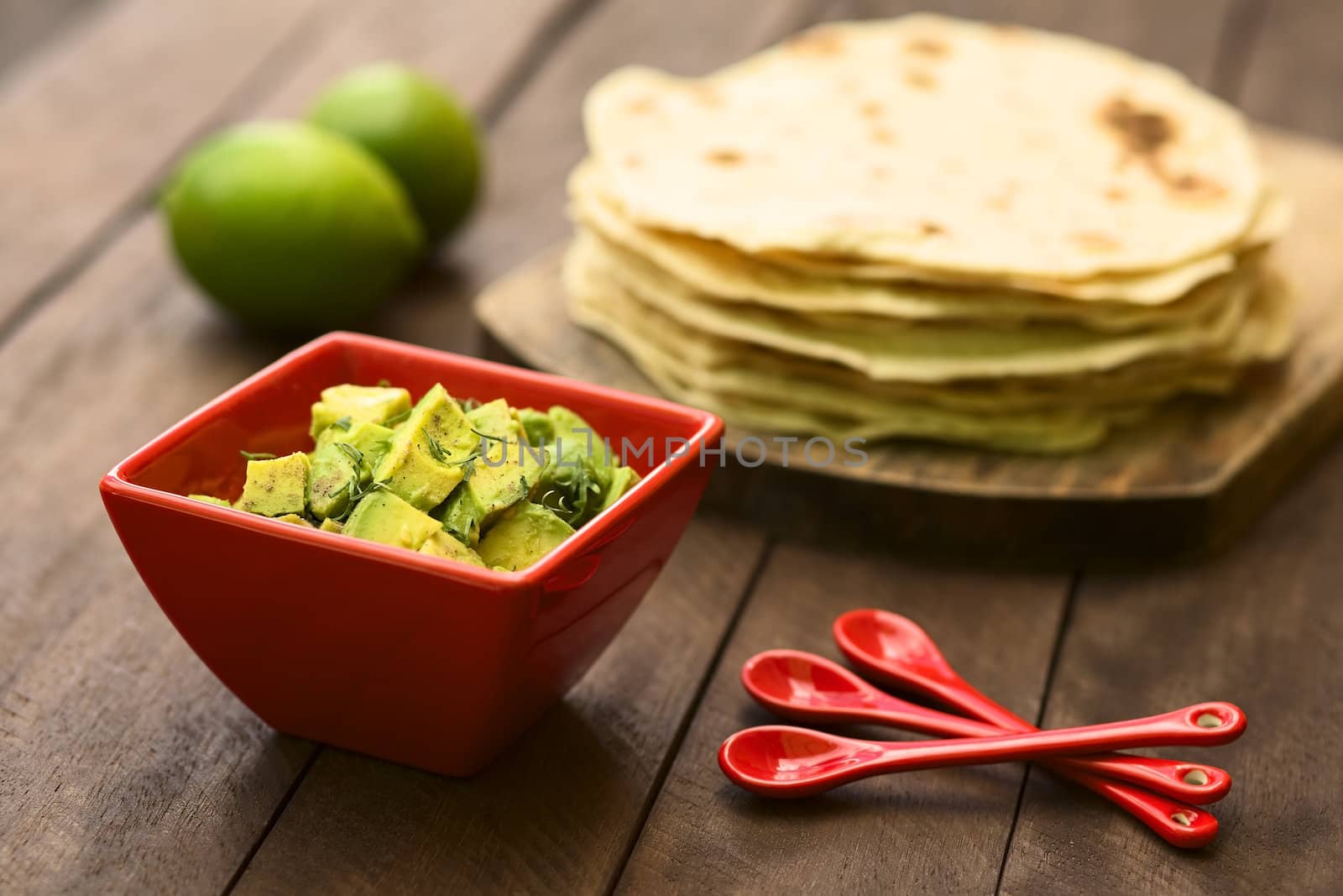 Fresh avocado salad prepared with lime juice, pepper, salt and sprinkled with fresh coriander leaves, homemade tortillas in the back (Selective Focus, Focus in the middle of the salad)  