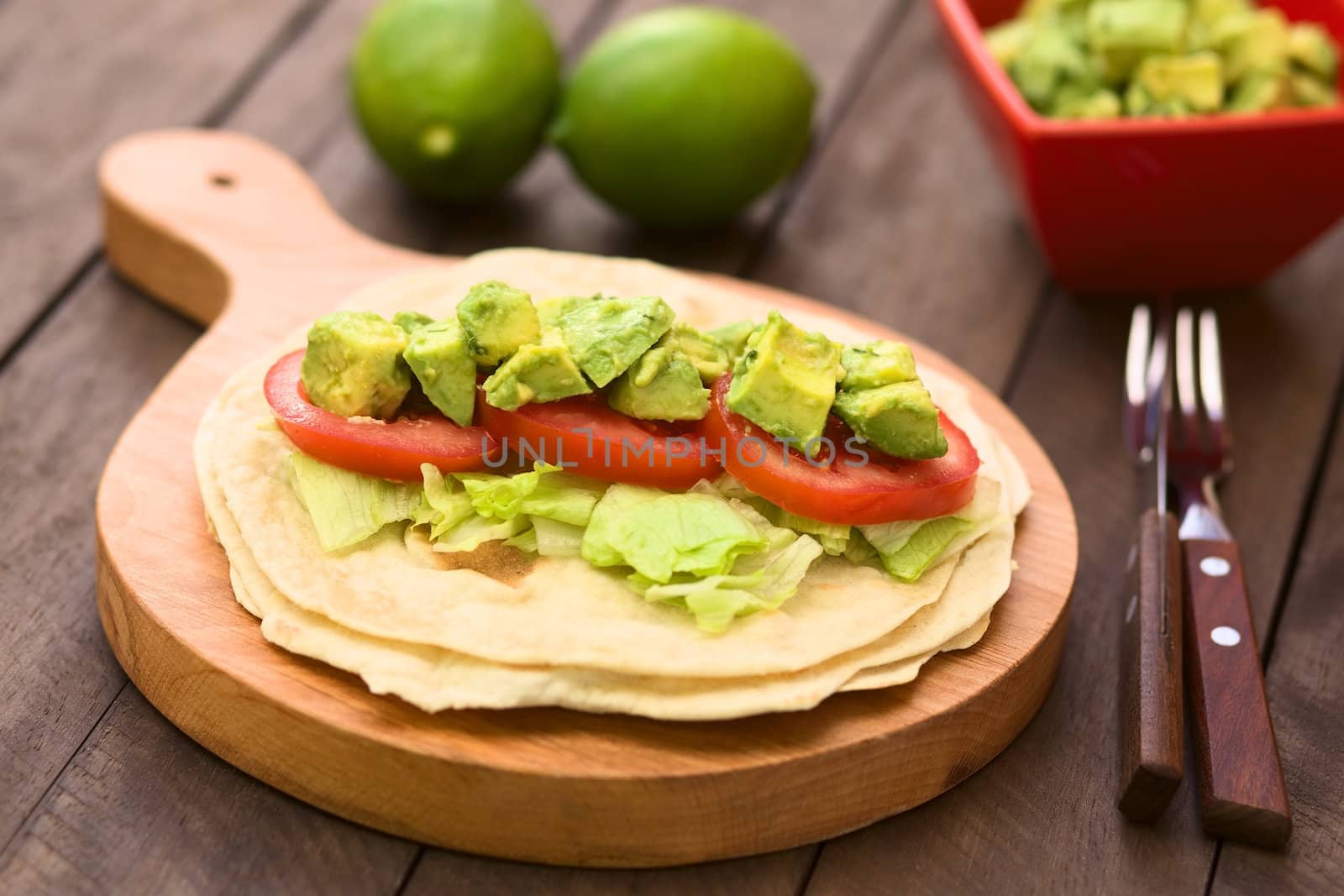 Fresh homemade tortilla with lettuce, tomato and avocado on wooden board (Selective Focus, Focus on the front of the avocado pieces on top)