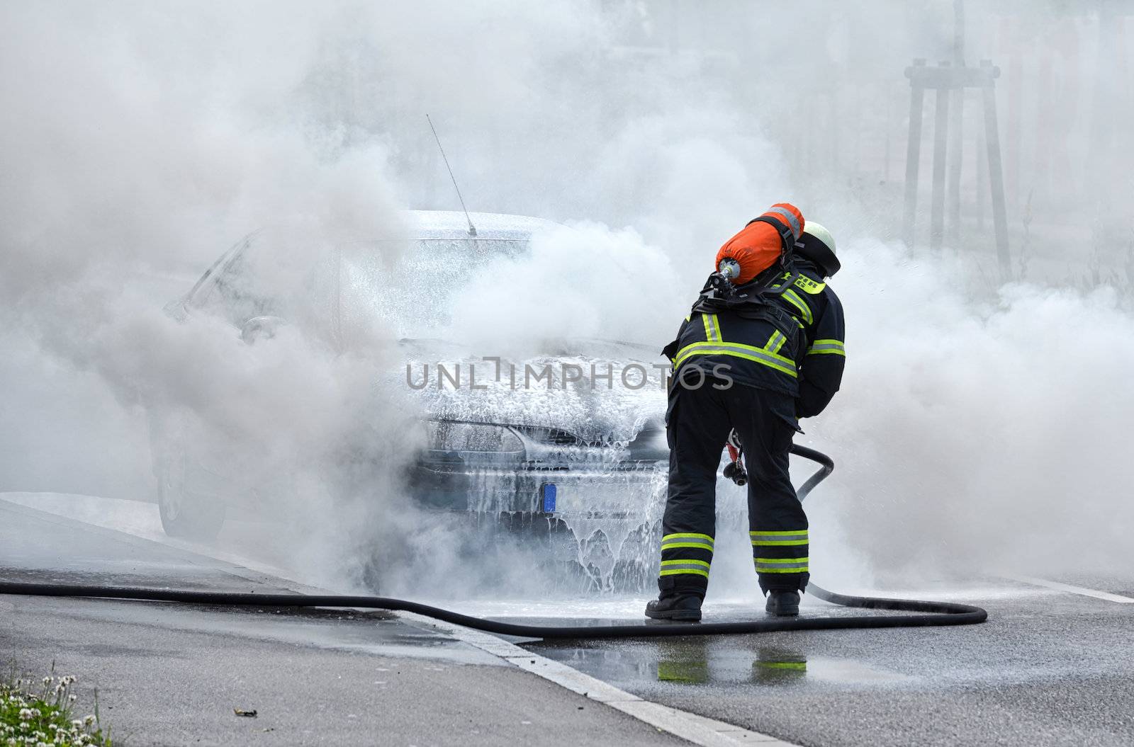 Burning motor vehicle been put out by fireman in protective clothing